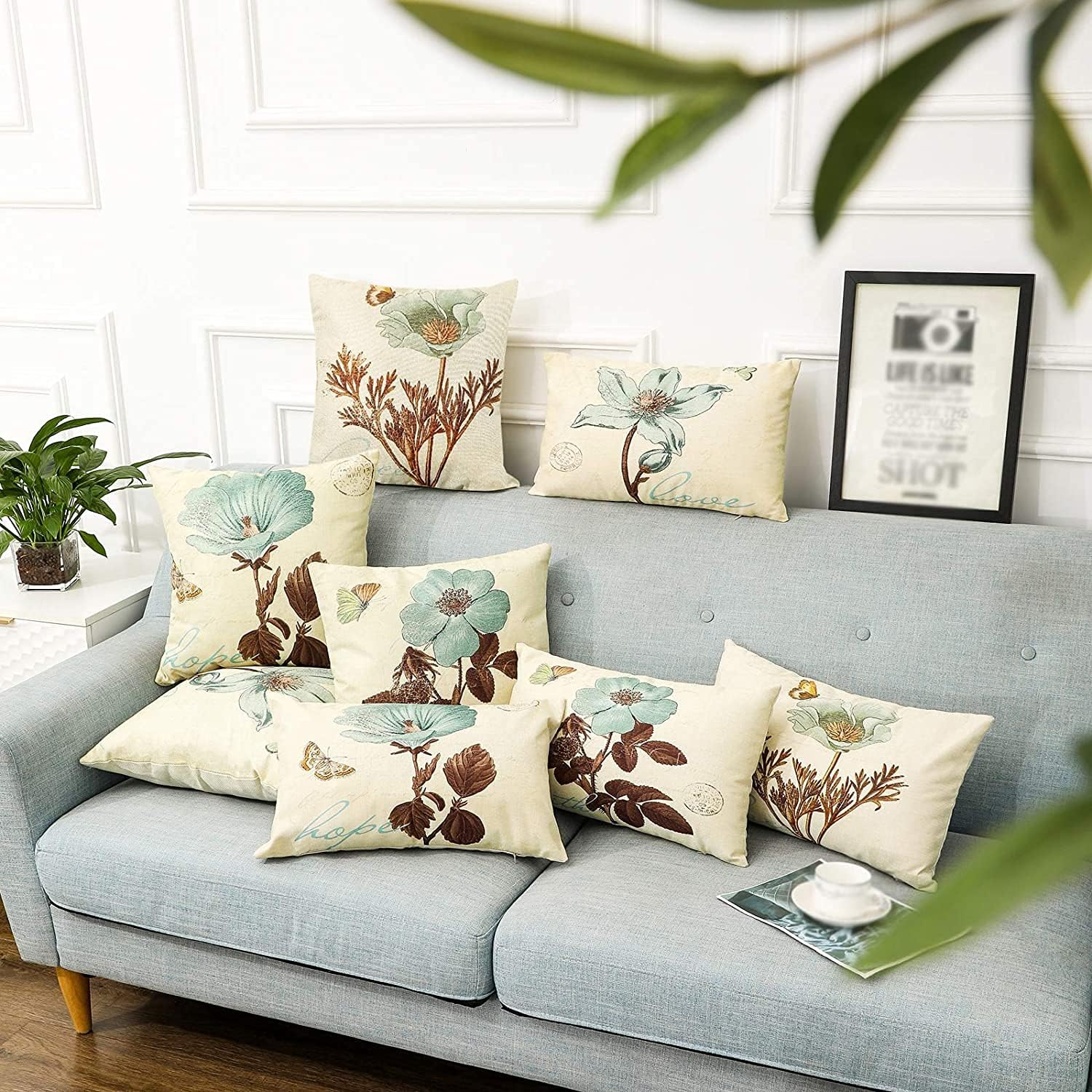 Ein Sofa mit mehreren Kissen. Jedes Kissen hat ein Blumendesign. Ein Bilderrahmen ist im Hintergrund.
