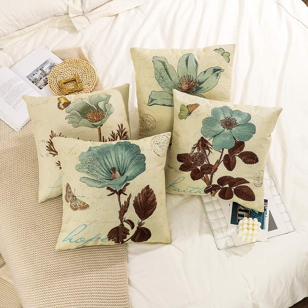 Vier quadratische Kissen mit Blumendruck auf einem Bett. Die Kissen haben hellblaue und beige Farben.