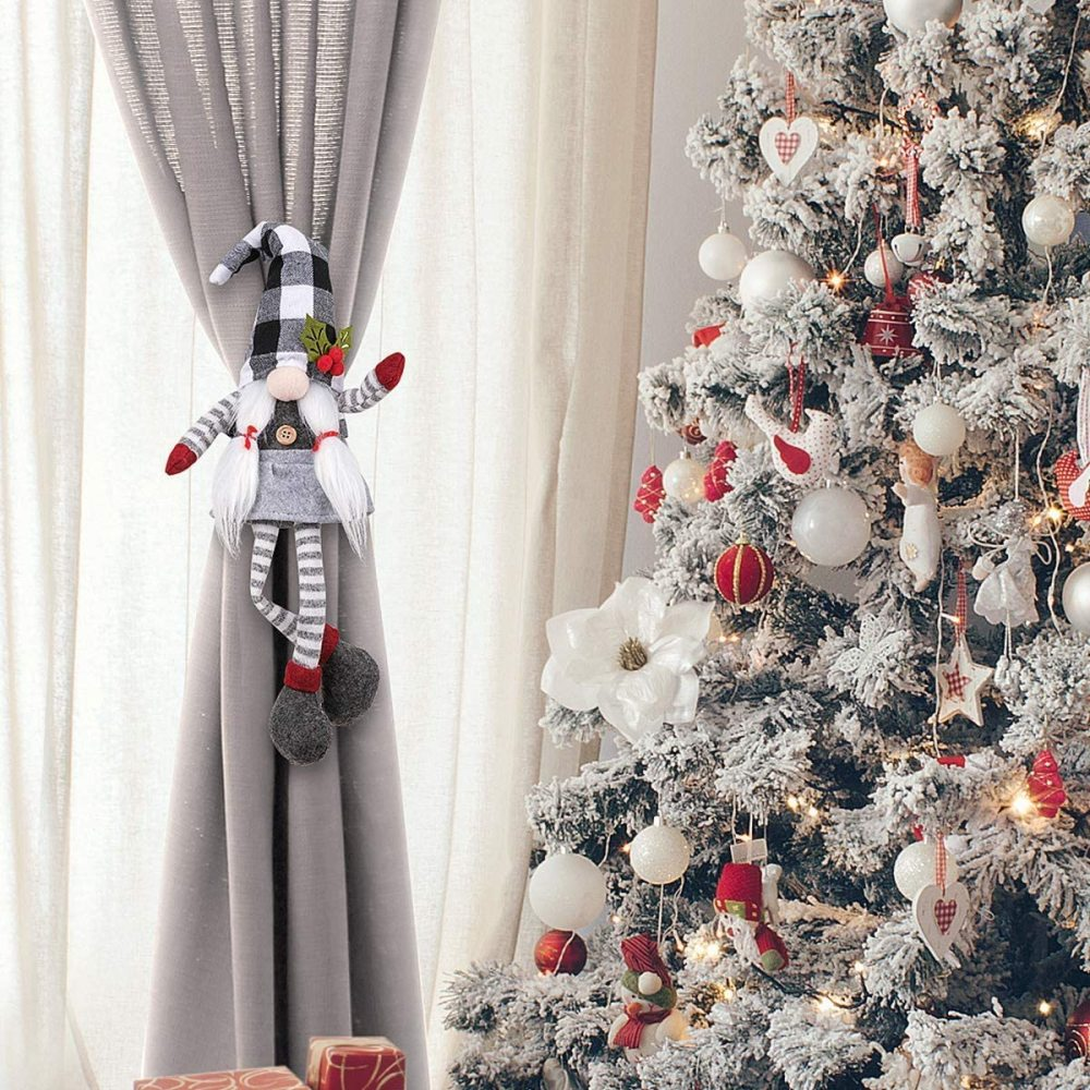 Ein Weihnachtsbaum mit Ornamenten und ein Zwerg-Gardinenhalter, der an einem grauen Vorhang hängt.