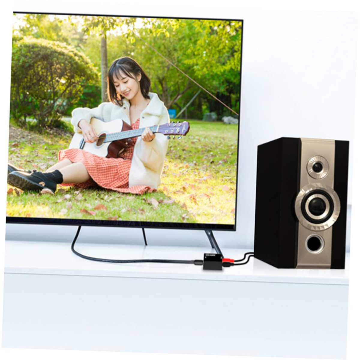 Eine Frau spielt Gitarre vor einem Fernseher, mit einem schwarzen Audio-Konverter und Lautsprecher daneben.