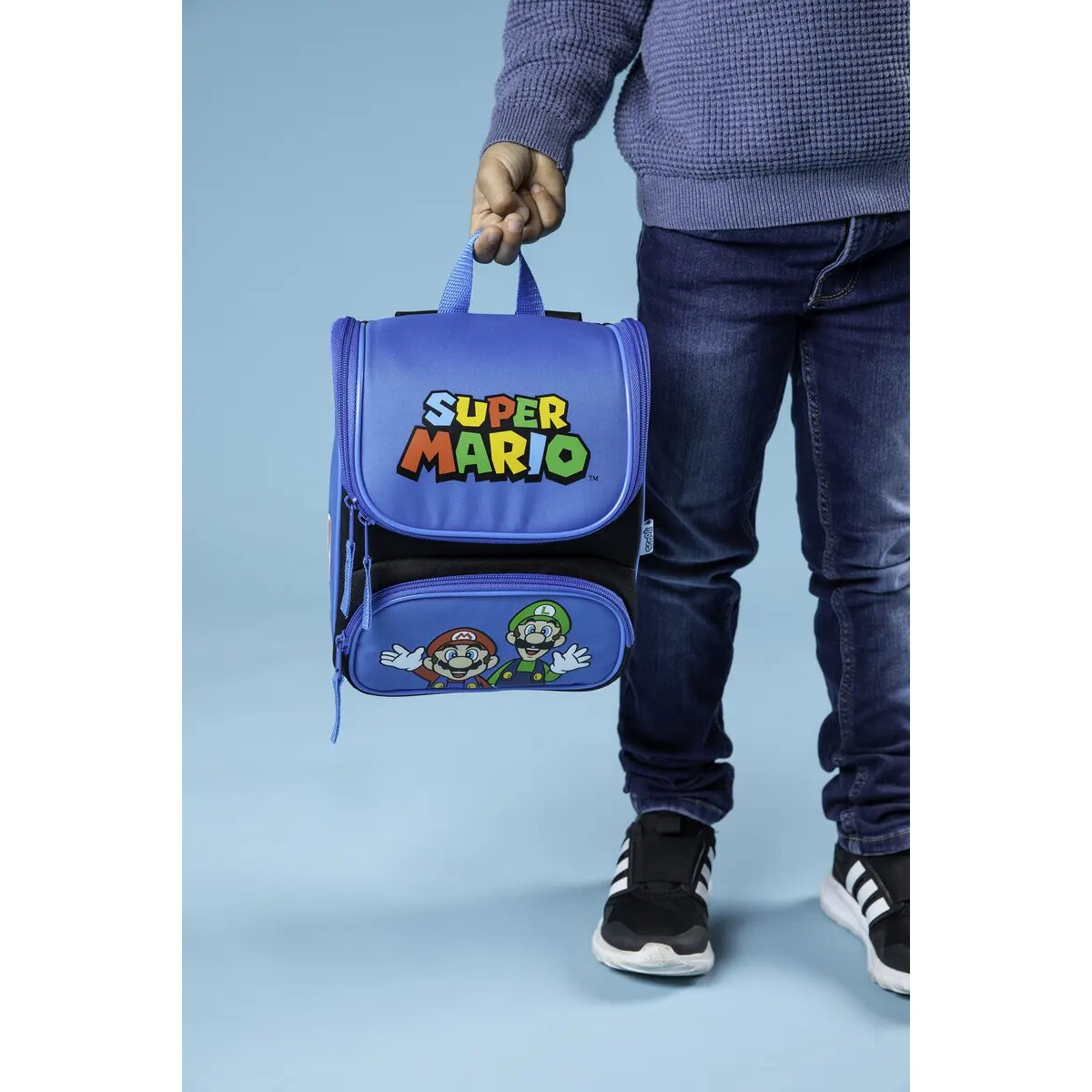 Een kind houdt een blauwe Super Mario lunchtas vast. De tas heeft een Super Mario logo en personages.