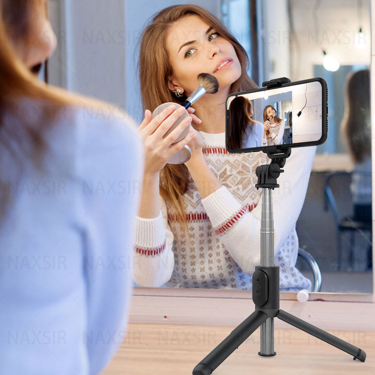 Eine Frau, die Make-up aufträgt, während sie auf ein Telefon blickt, das an einem Selfie-Stick mit Stativ befestigt ist.