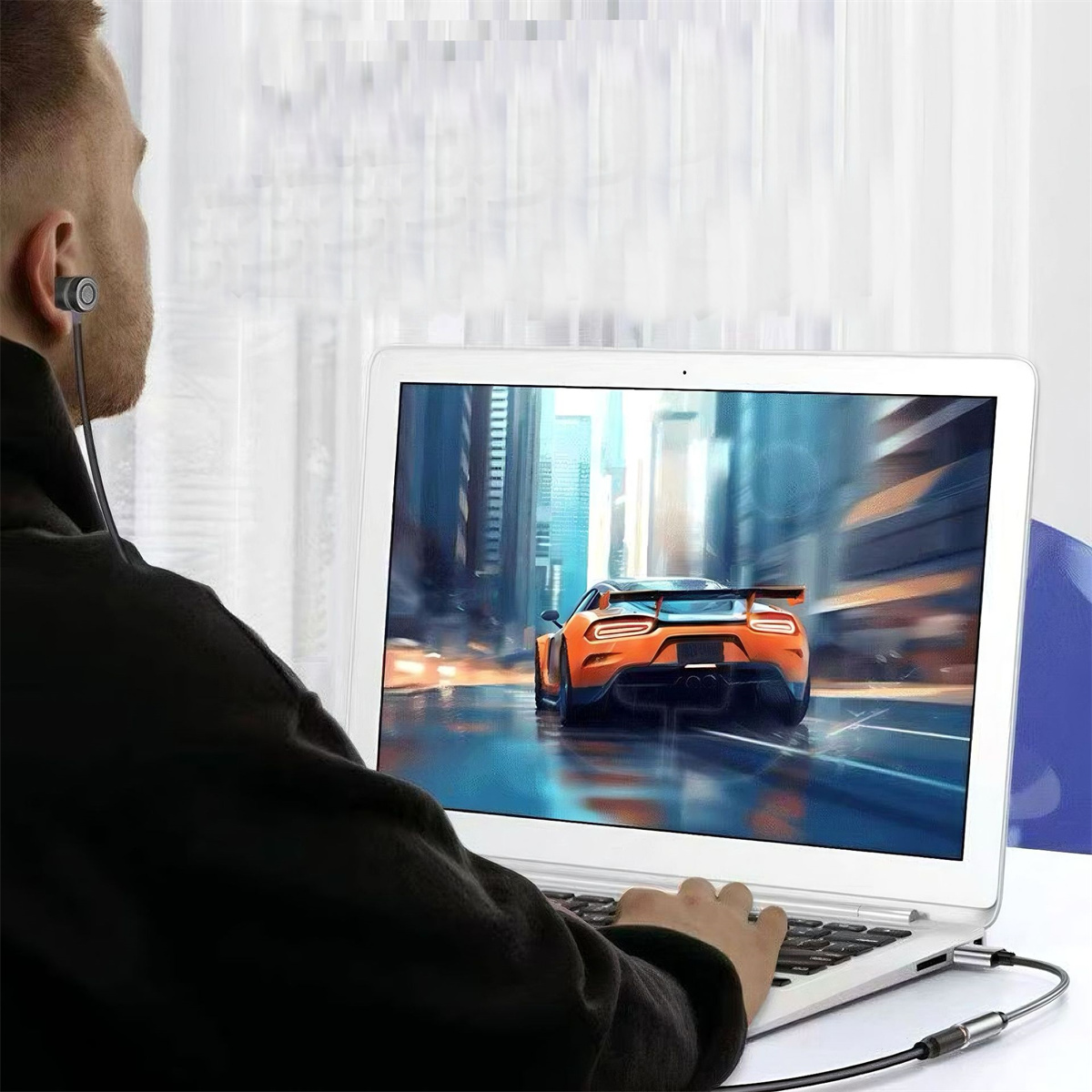 Mann mit Kopfhörern benutzt einen Laptop. Der Bildschirm zeigt ein oranges Auto auf nasser Straße.