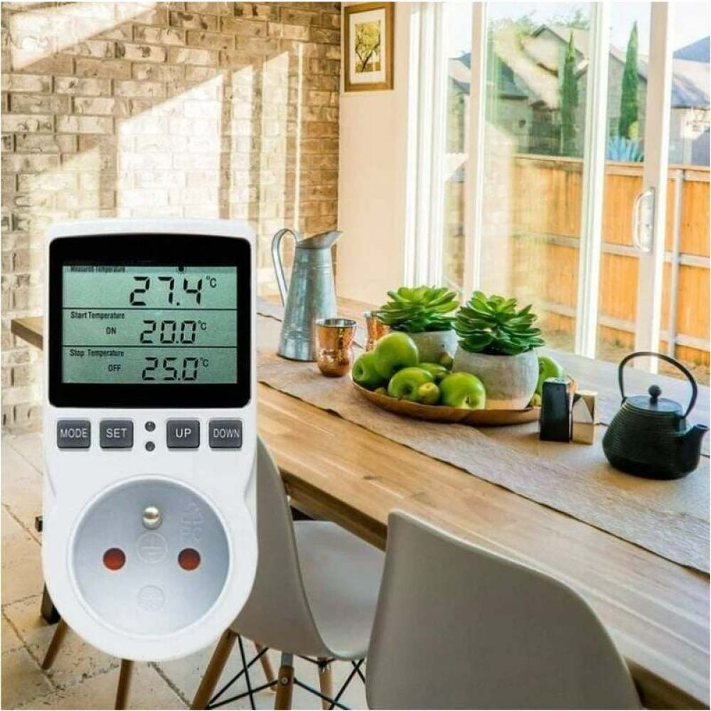 Ein digitaler Temperaturregler mit Messwerten und Stecker, platziert auf einem Tisch mit Pflanzen und Deko.