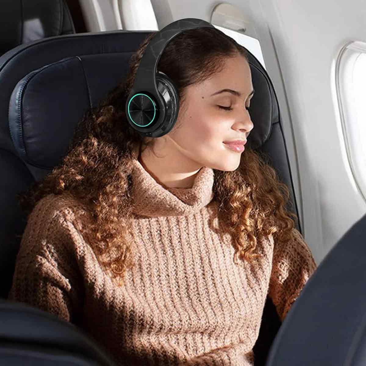 Eine Frau mit schwarzen Kopfhörern im Flugzeug, lächelnd, während sie aus dem Fenster schaut.