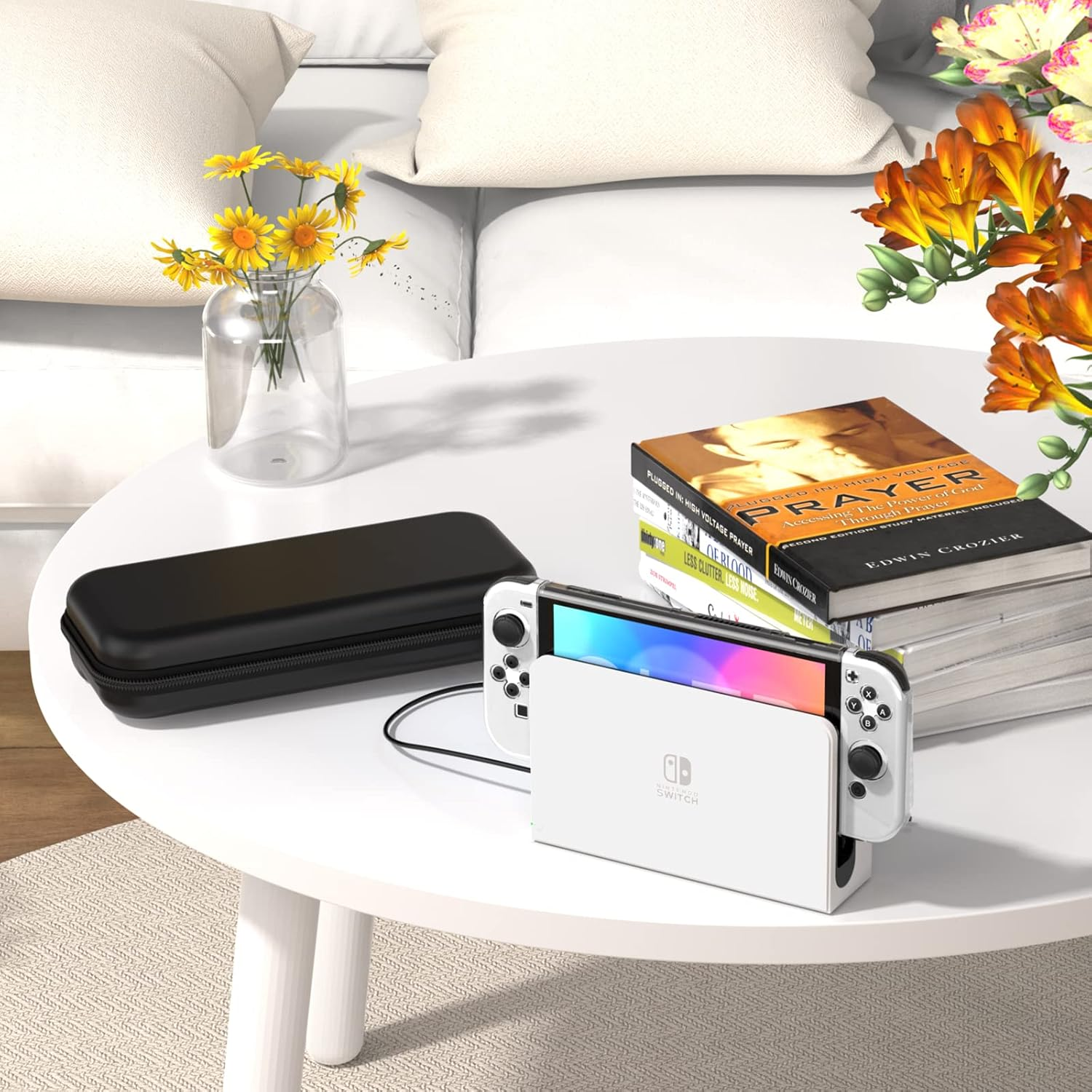Weiße Switch in Dock auf einem Tisch. Schwarze Hülle, Blumen, Bücher. Couch und Kissen im Hintergrund.