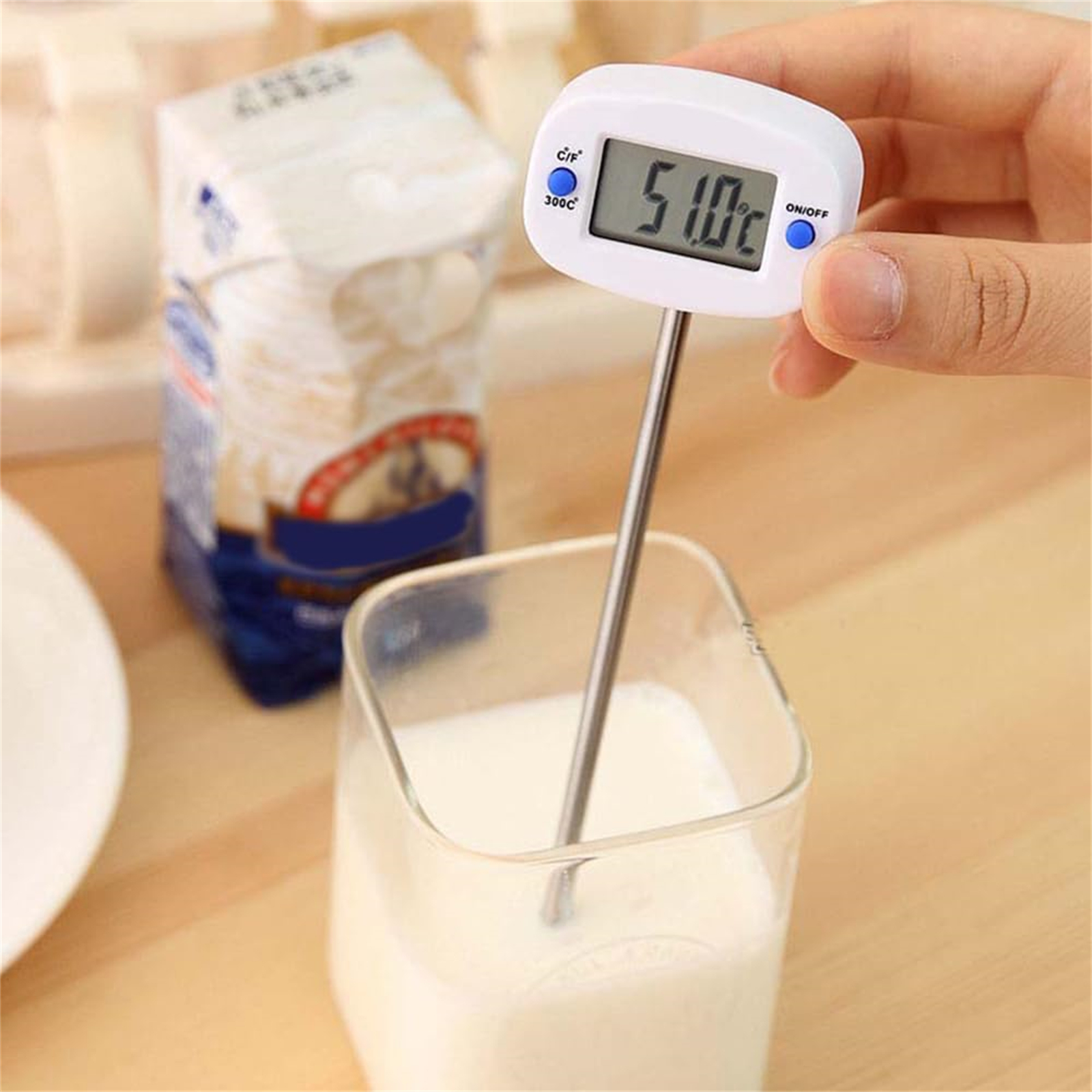 Thermometer in Milch. Glas mit Milch, weißes Thermometer zeigt 51,0 Grad. Hintergrund ist unscharf.