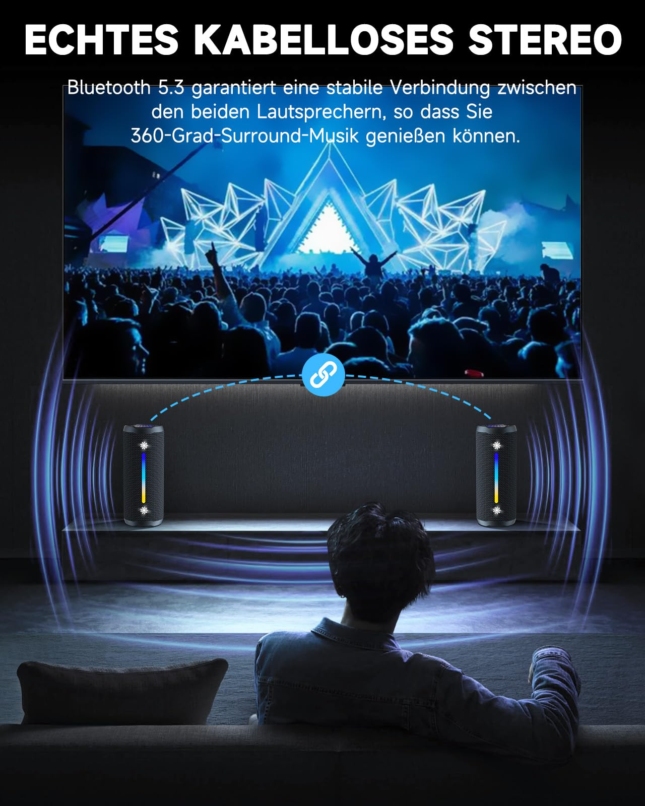 Zwei schwarze Lautsprecher mit einem Fernseher im Hintergrund, eine Person sitzt auf dem Sofa.