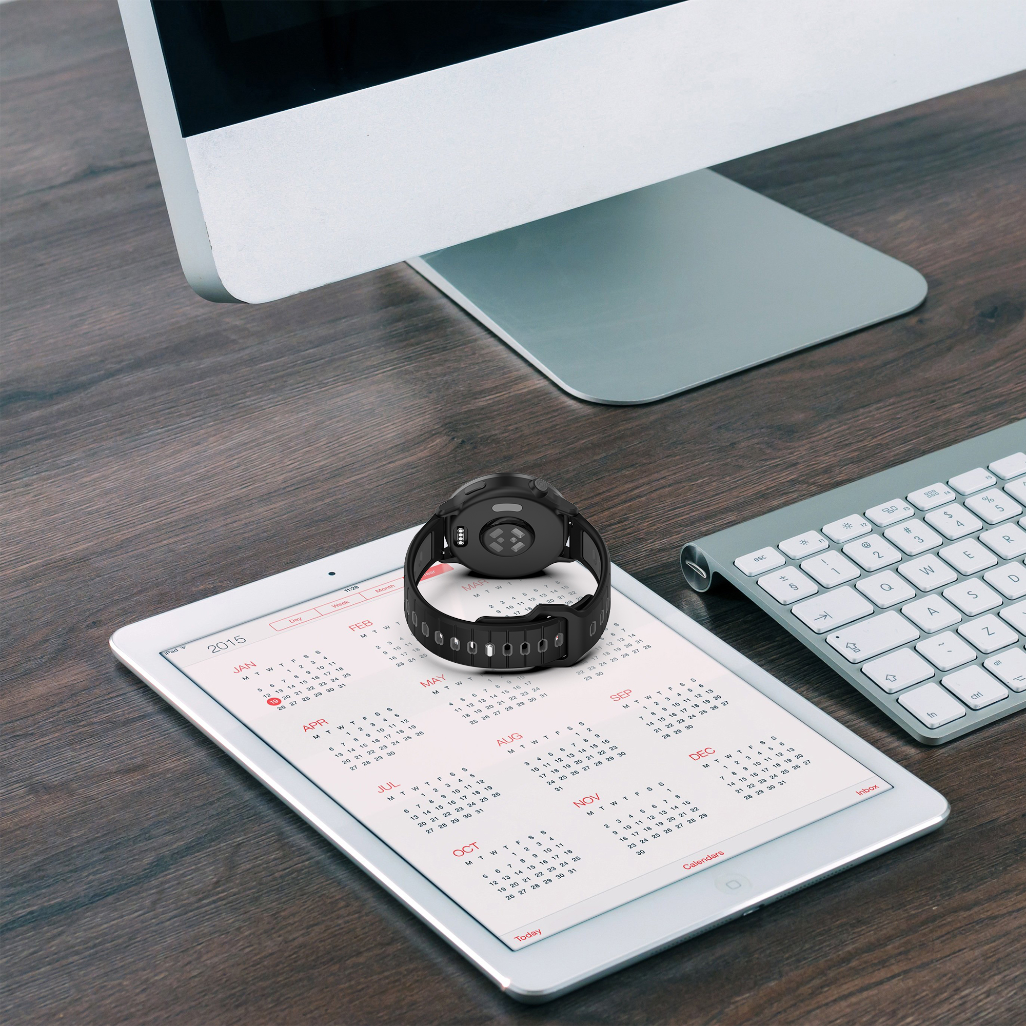 Smartwatch auf einem geöffneten Tablet mit Kalenderansicht und Tastatur im Hintergrund.