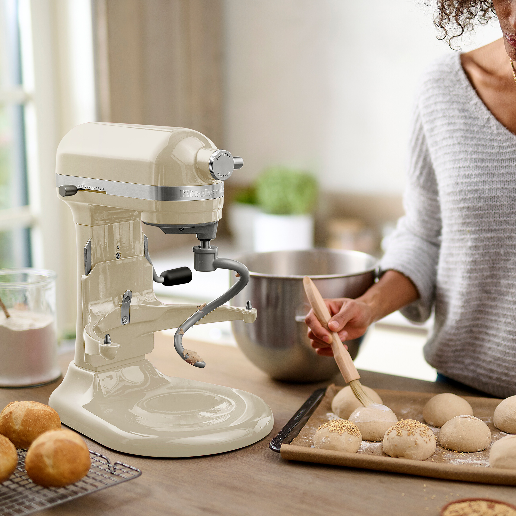 Eine Frau benutzt einen cremefarbenen KitchenAid-Mixer. Sie bestreicht Teig mit einem Pinsel.