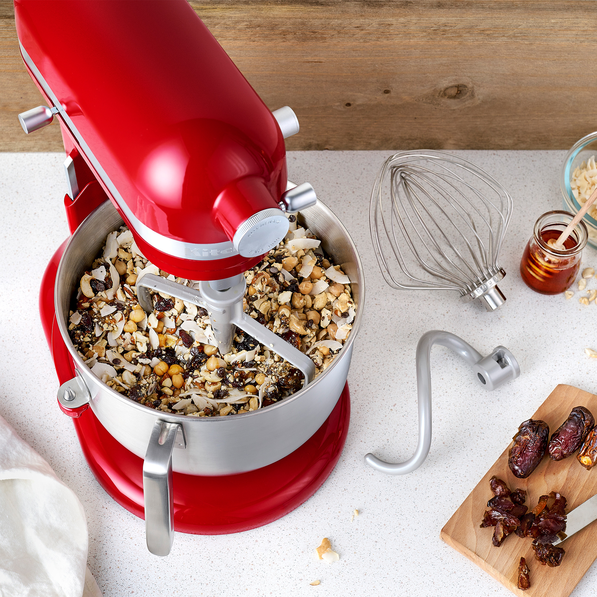 Ein roter KitchenAid-Mixer mit Zutaten in der Schüssel. Andere Werkzeuge und Zutaten sind in der Nähe.