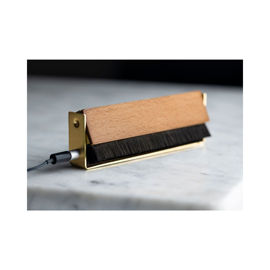 Mała szczotka z drewnianą nakładką do czyszczenia z metalową ramą w kolorze złotym. Podłączony jest czarny kabel.