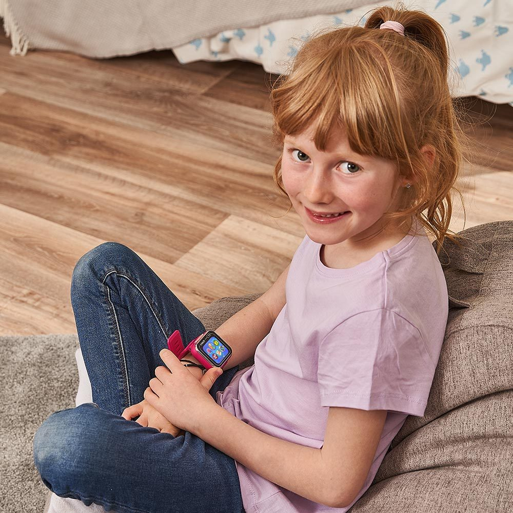 Ragazza con capelli rossi in una coda di cavallo che indossa uno smartwatch rosa, seduta su un cuscino e sorridente.