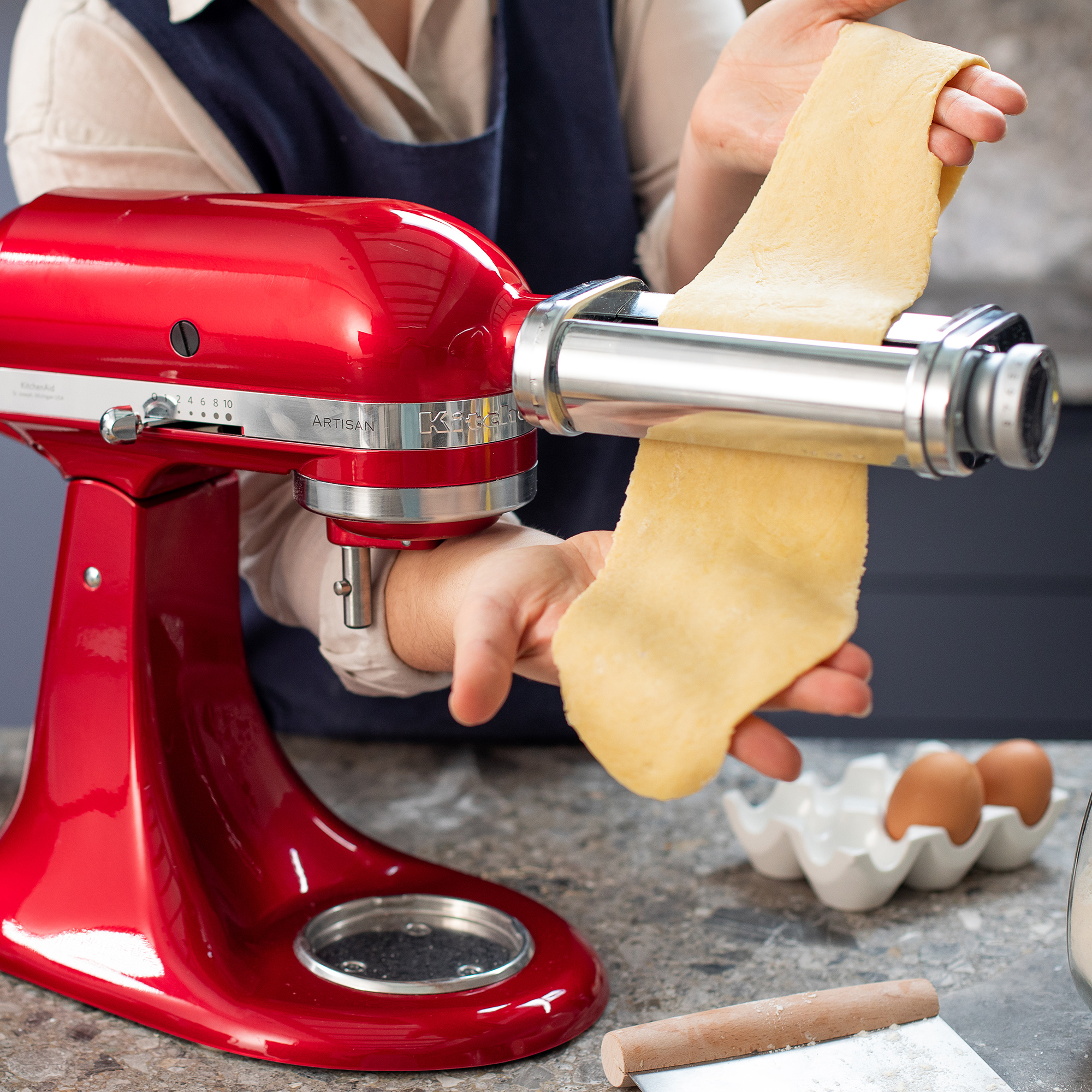 Red KitchenAid mixer with pasta maker in use, pasta being made.