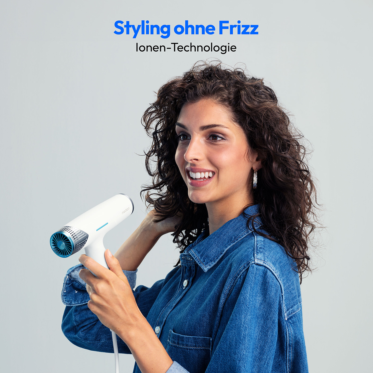 Kobieta trzymająca białą suszarkę do włosów, uśmiechnięta, z tekstem u góry. Jasne tło.