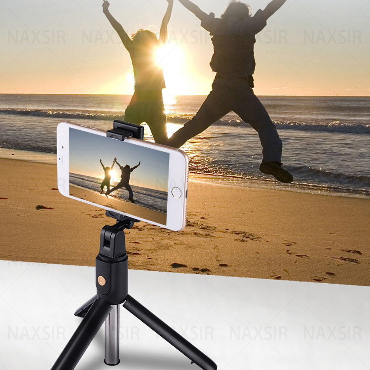 Ein Telefon auf einem Stativ macht ein Foto. Zwei Personen springen am Strand bei Sonnenuntergang.