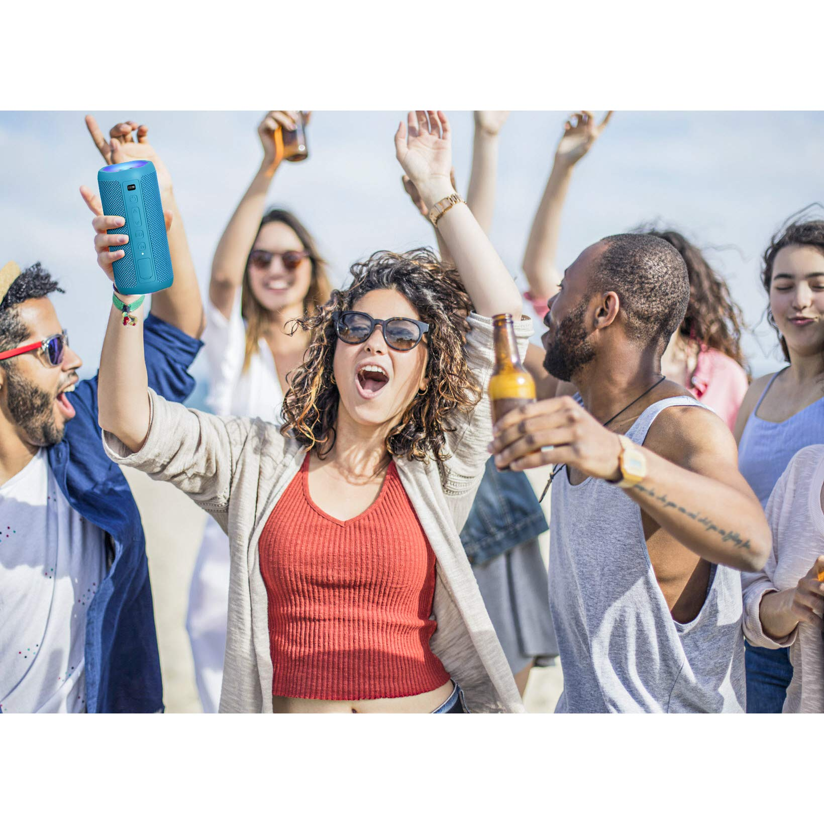 Menschengruppe am Strand, eine Frau hält einen blauen Lautsprecher, andere tanzen.