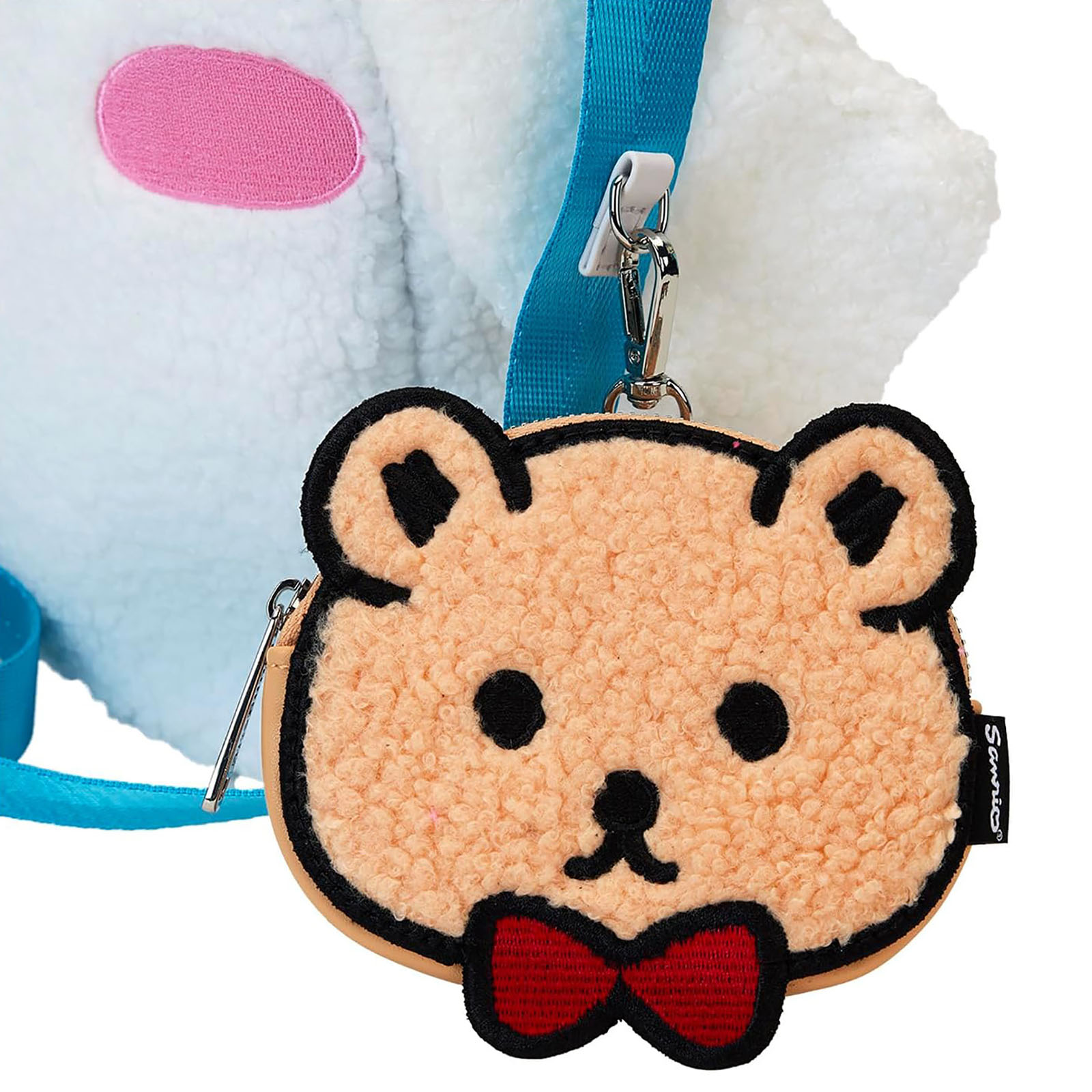 Nahaufnahme eines Bären-Münzbeutels mit roter Schleife neben einer weißen Cinnamoroll-Tasche.