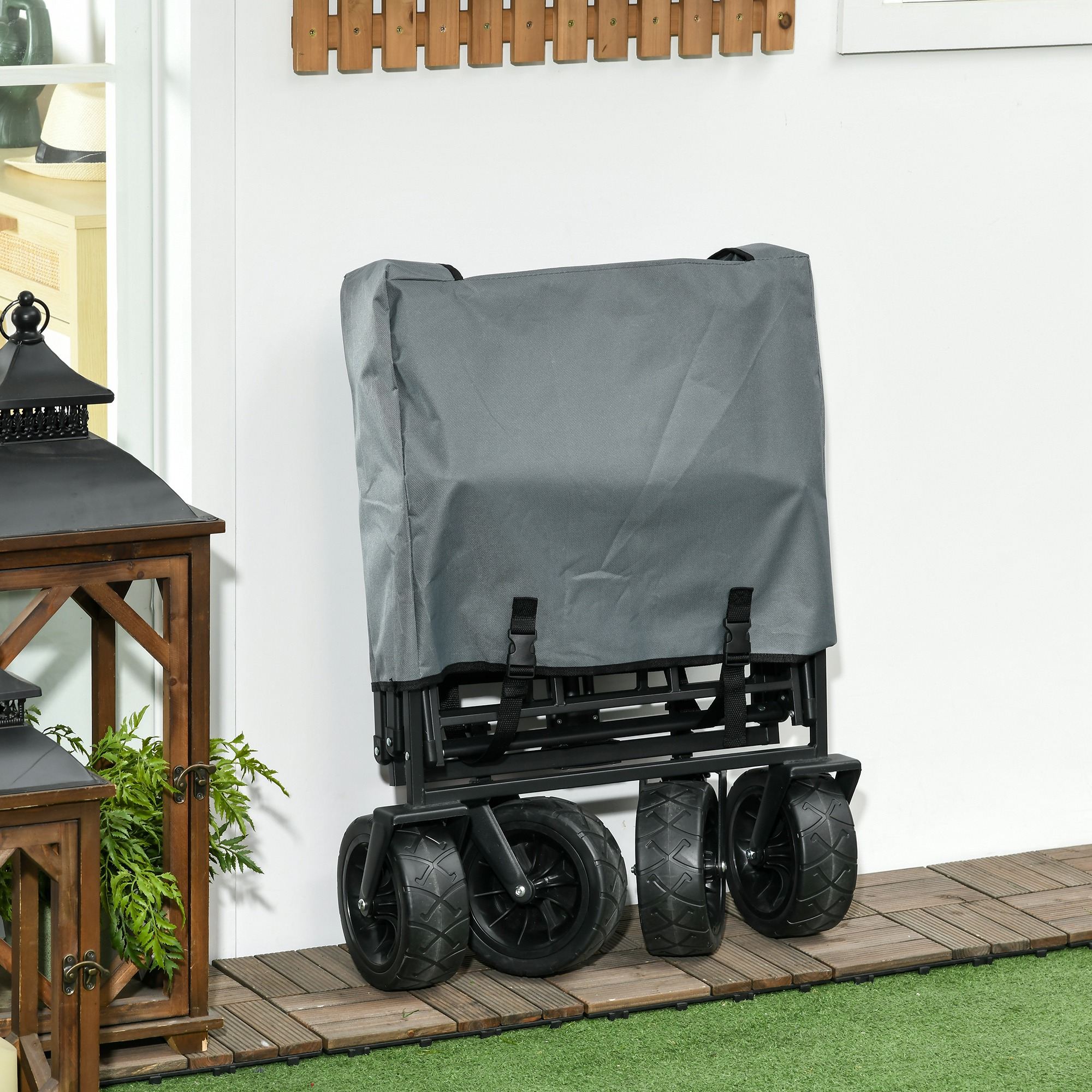 Grauer faltbarer Wagen, schwarze Räder, steht an einer weißen Wand auf Holzplanken.