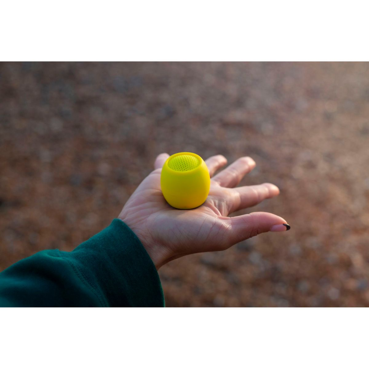 Altoparlante giallo e rotondo tenuto in mano. Scatto all'aperto, sfondo sfocato.