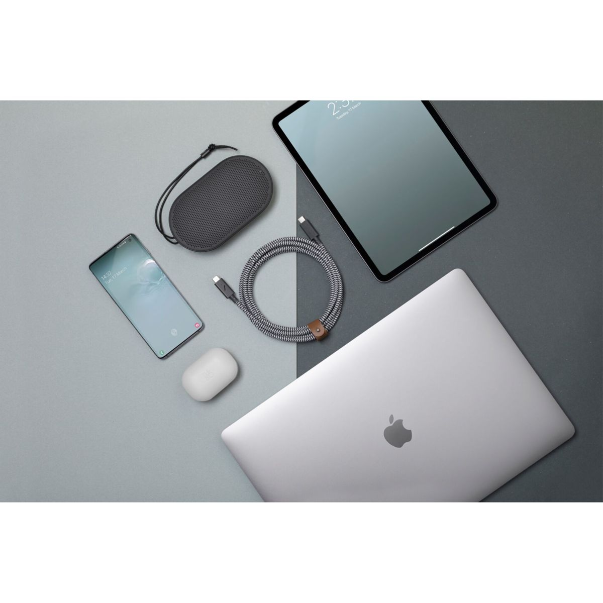 Configurazione tecnologica: telefono, altoparlante, cavo, tablet, laptop. Sfondo grigio.