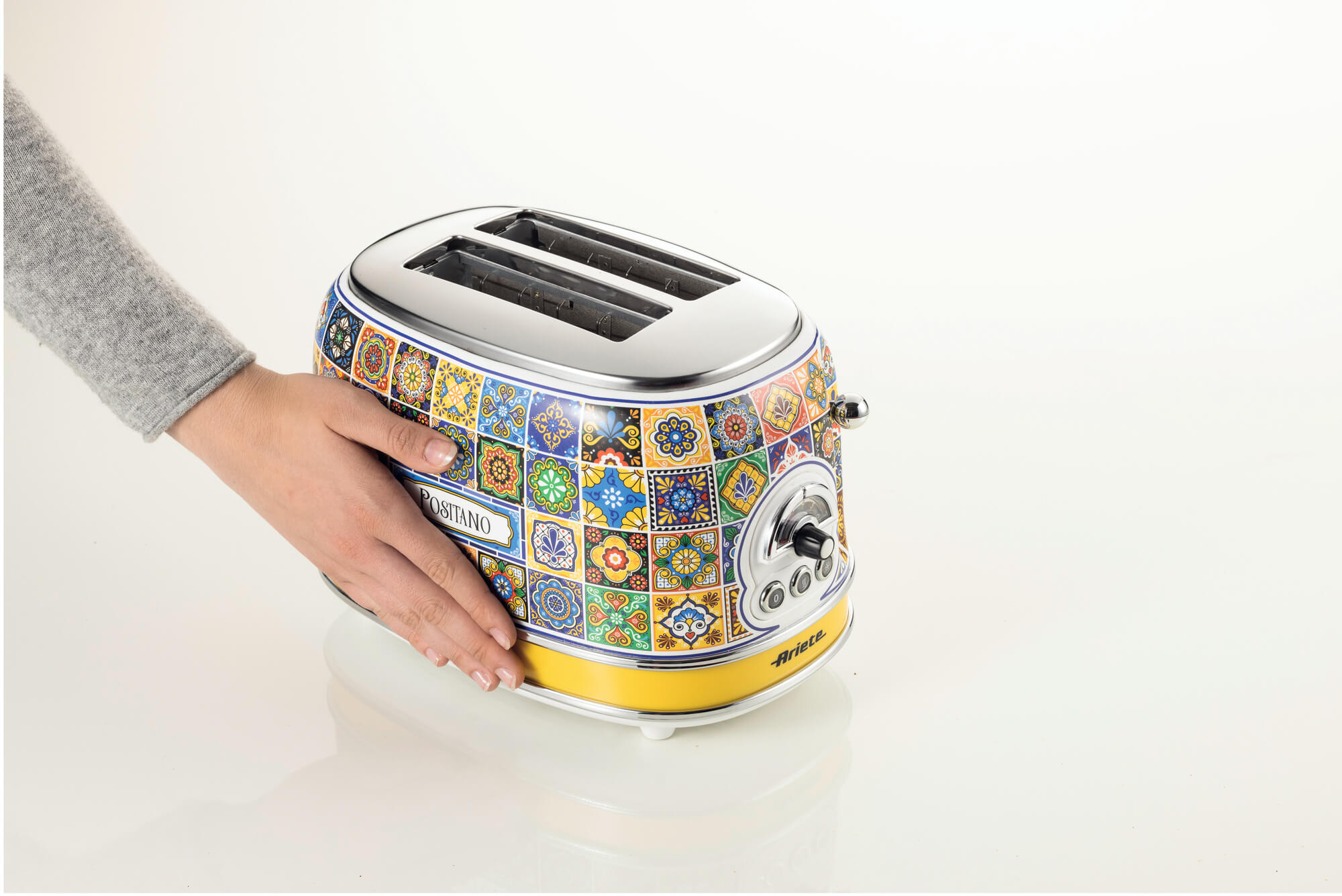 Kolorowy, wzorzysty toster z nazwą 'Postano' i marką 'Ariete', obsługiwany przez osobę.