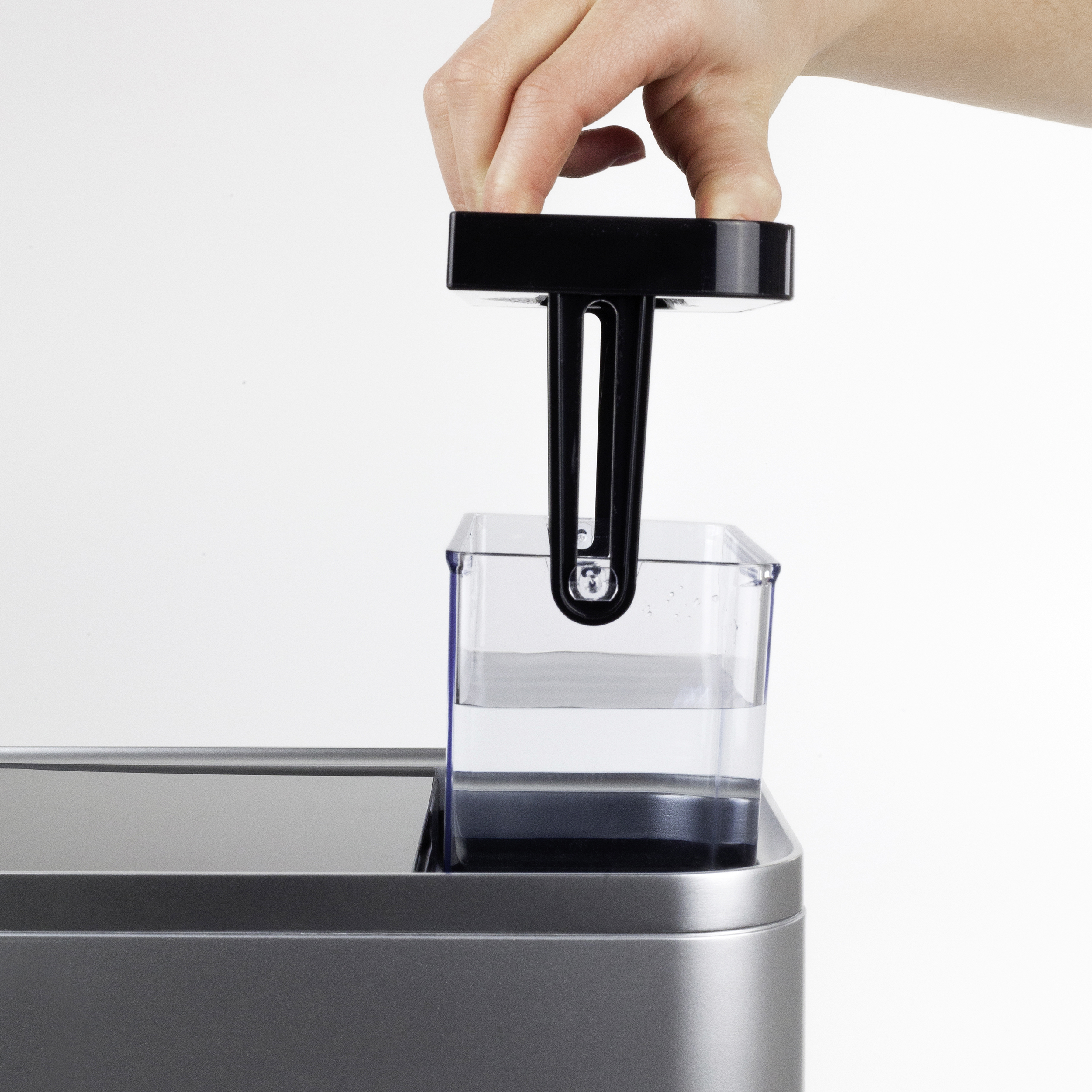 Hand, die einen schwarzen Griff in einen Wasserbehälter setzt.
