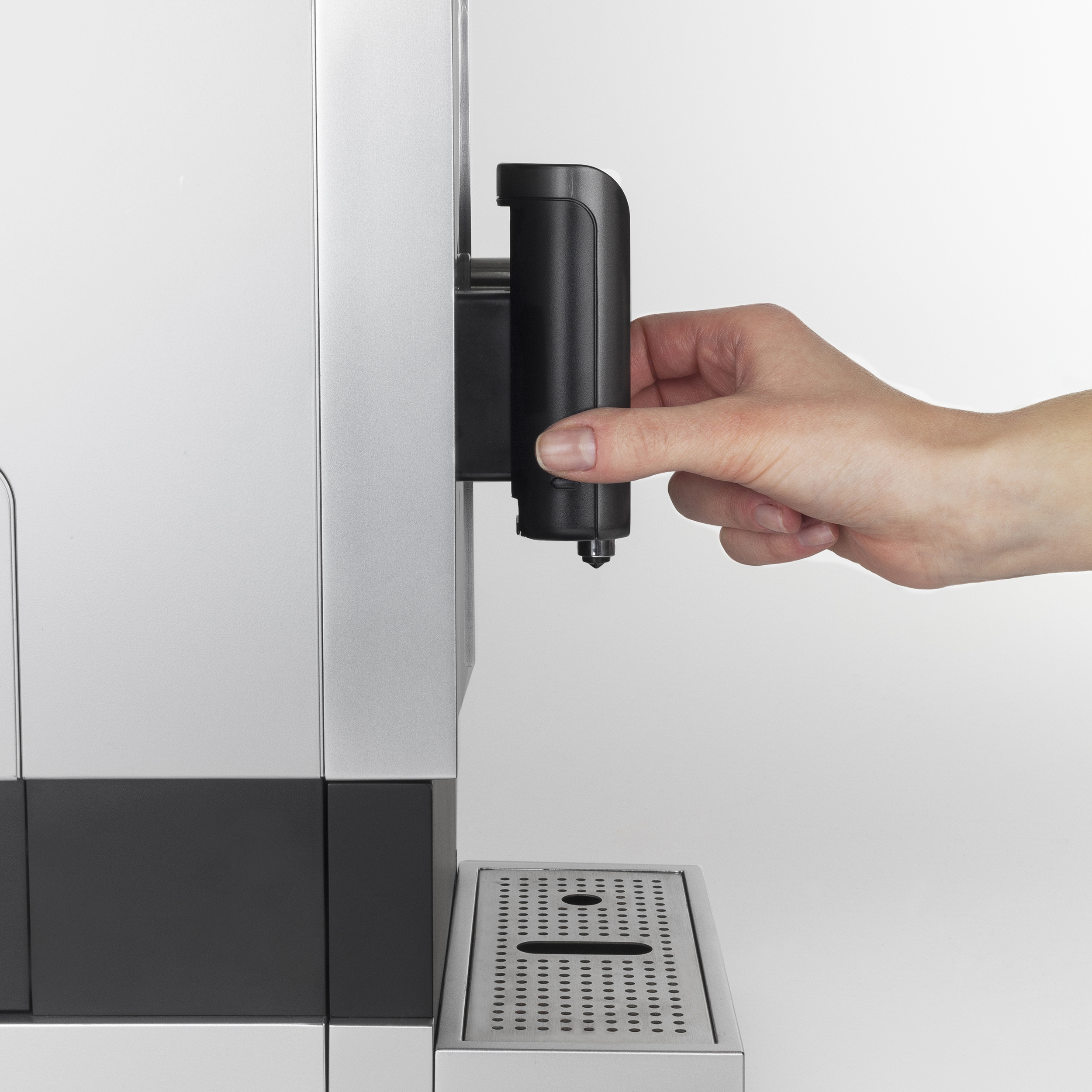Eine Hand greift nach einem schwarzen Teil einer weißen und silbernen Kaffeemaschine.