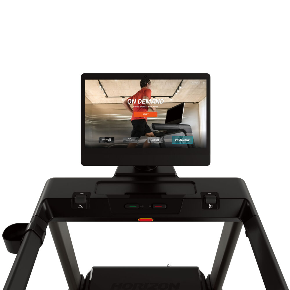 A treadmill with a screen displaying 'On Demand' and a person running. Black, white background.