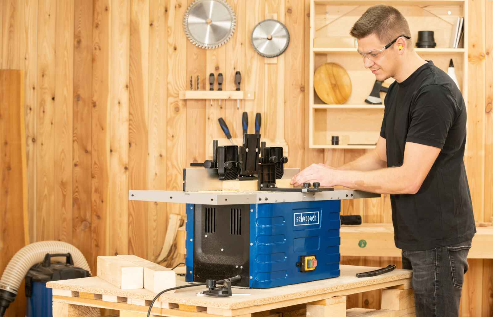 Uomo con occhiali e protezione per le orecchie che lavora con una macchina per la lavorazione del legno.