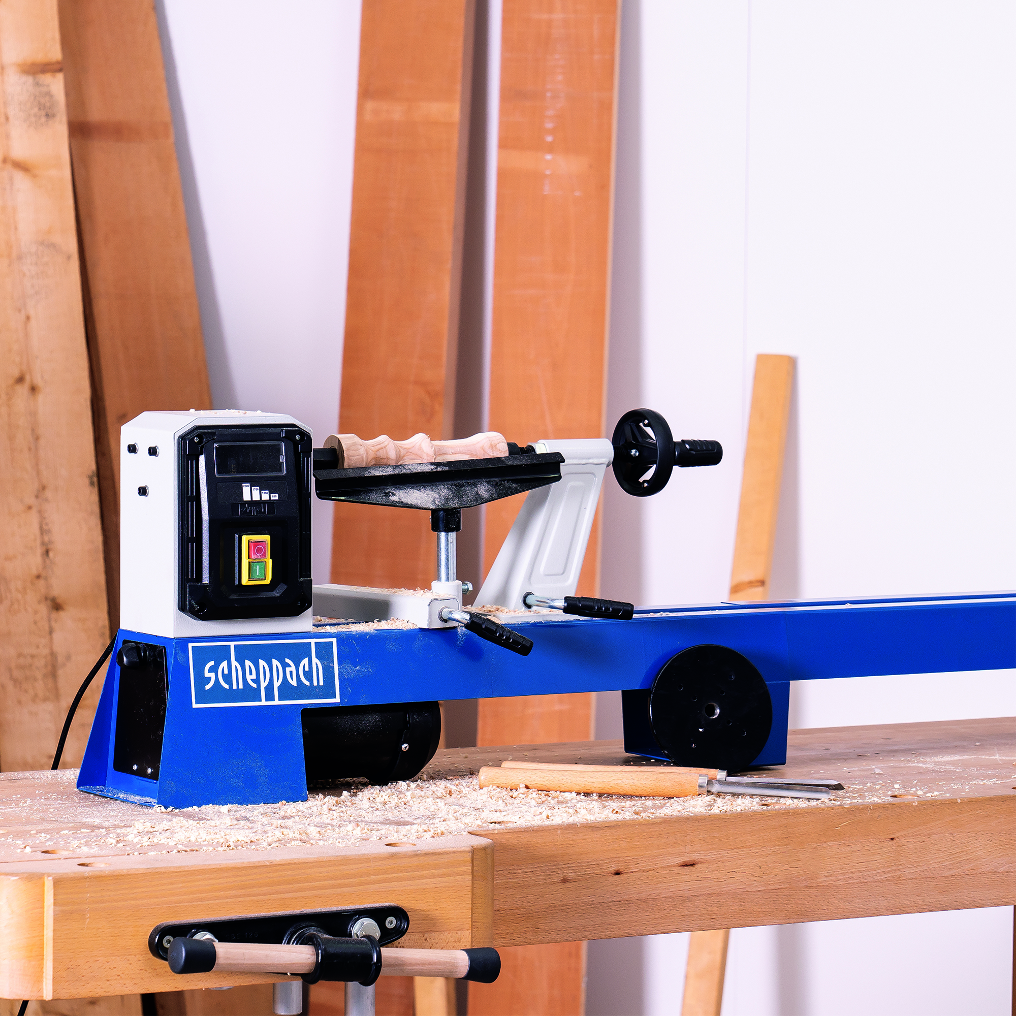 Tornio per legno, blu e bianco, con un pezzo di legno in lavorazione. Segatura copre il tavolo.