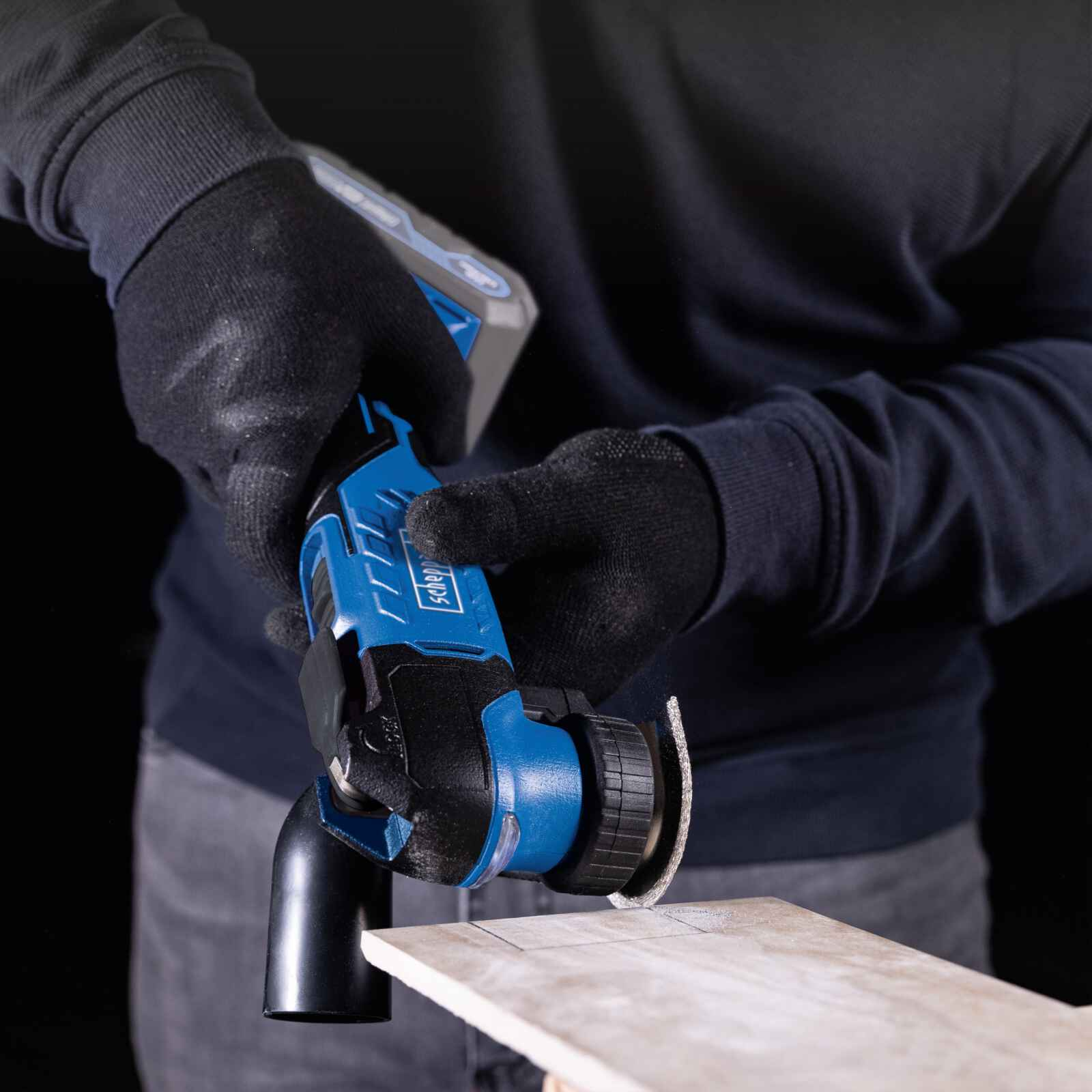 Una persona usa un utensile multifunzione oscillante blu e nero su una superficie di legno.