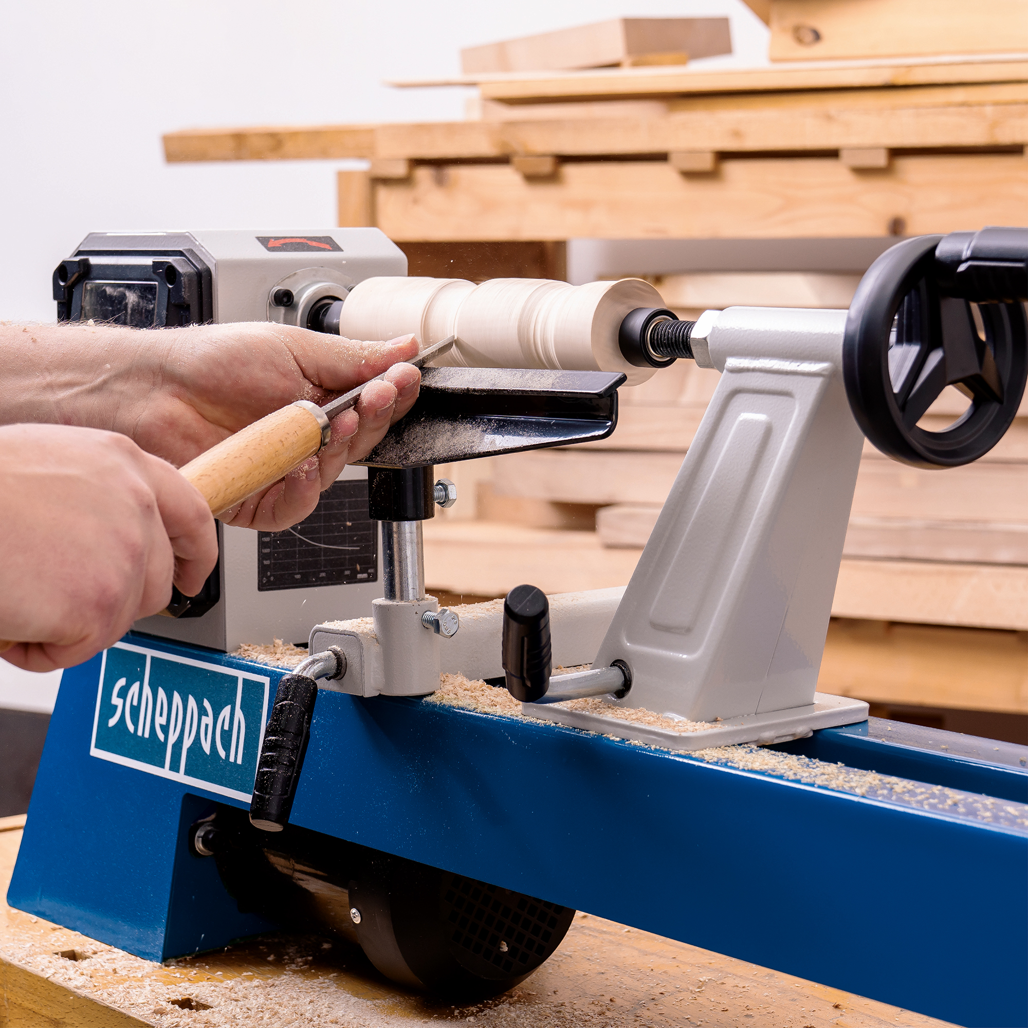 Persona che usa un tornio per legno. Il legno viene modellato con uno scalpello. Segatura visibile.