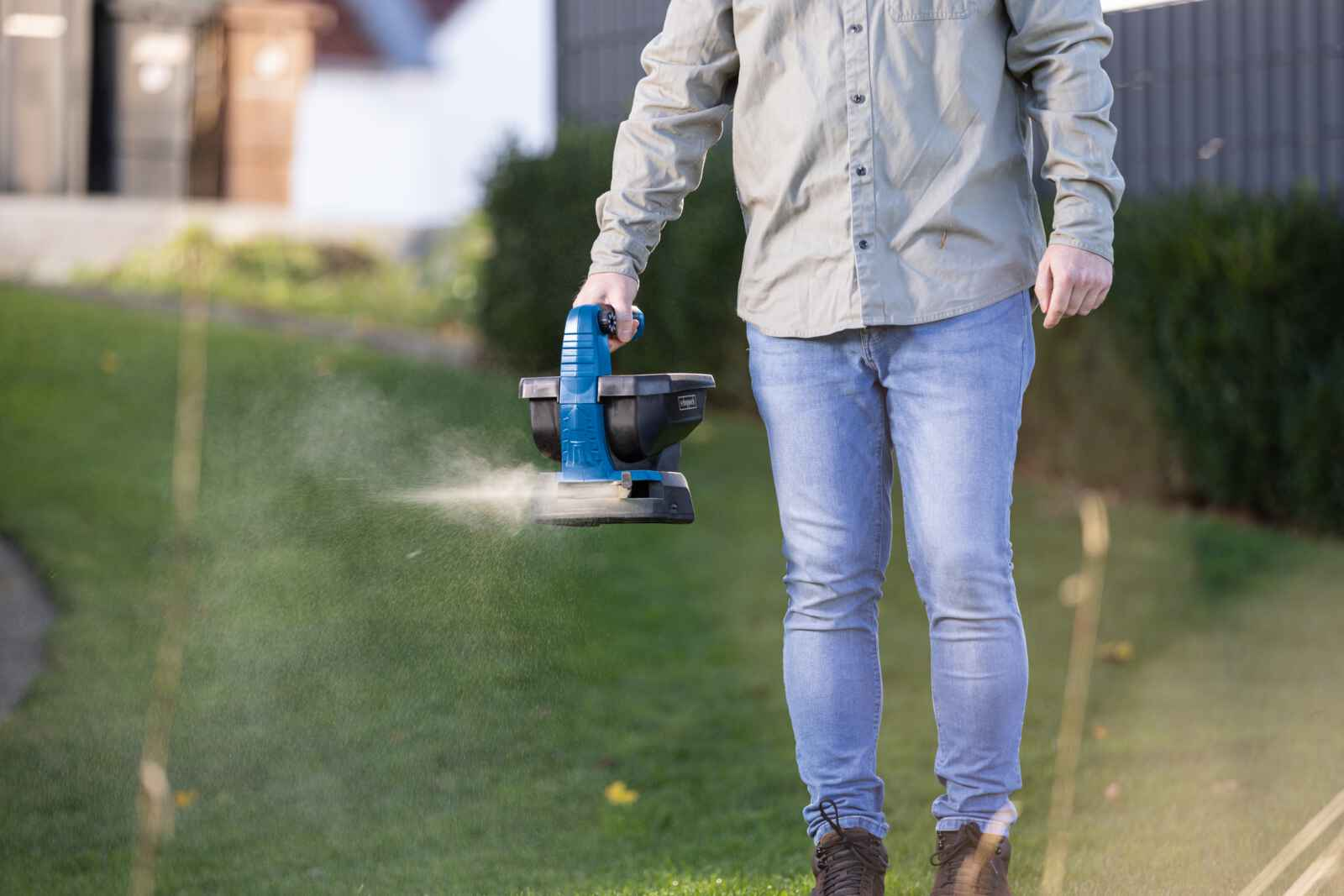 Una persona che sparge semi sull'erba con uno spargitore blu e nero.