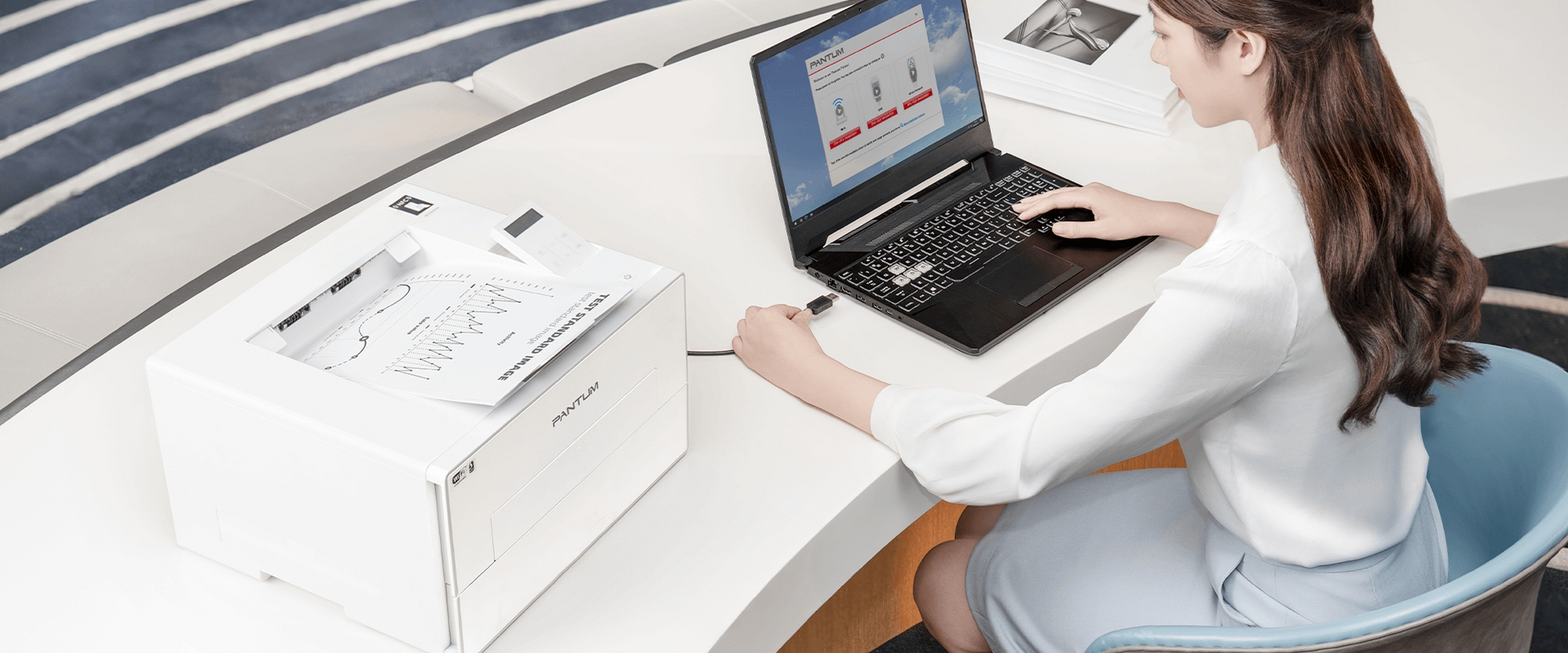 Kobieta korzystająca z laptopa, z drukarką i wydrukiem po lewej stronie na biurku.