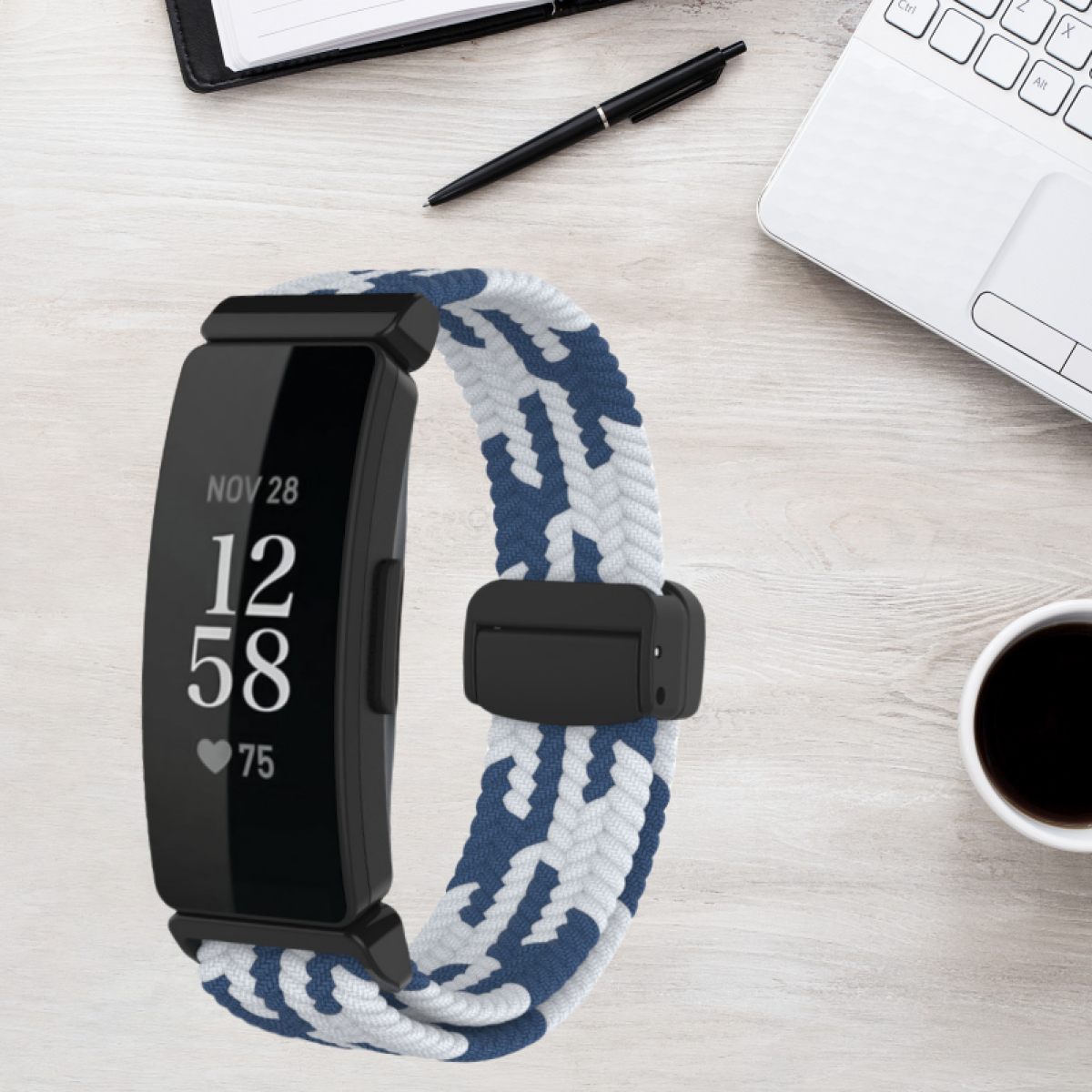 Schwarzer Fitnesstracker mit blau-weißem Armband auf einem Holztisch mit Laptop und Stift.