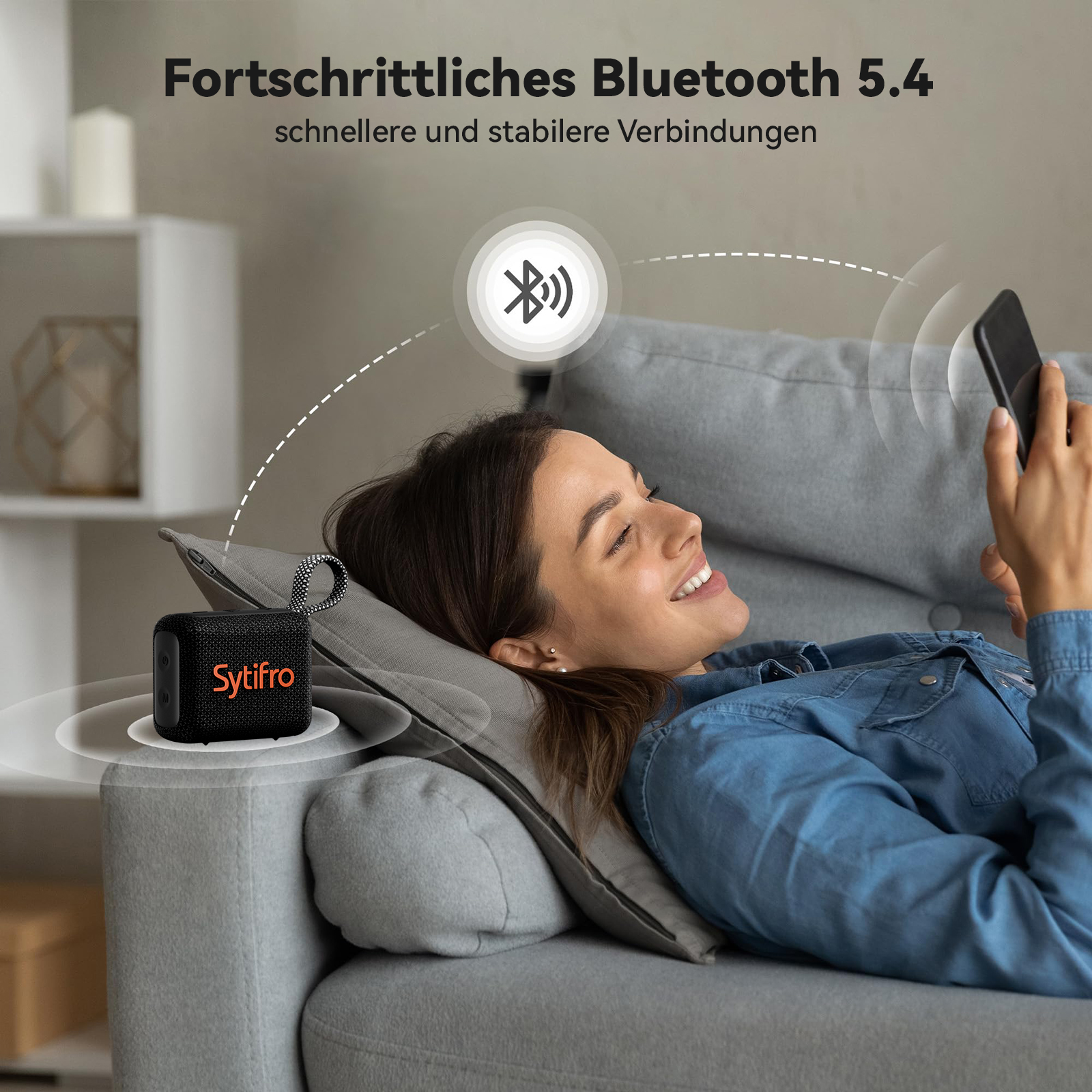 Frau liegt auf Sofa, nutzt Smartphone. Kleiner schwarzer Lautsprecher mit dem Markennamen Sytifro.