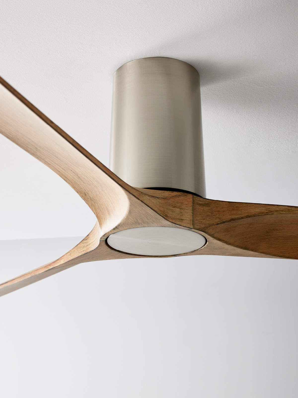 Deckenventilator mit drei Holzflügeln. Silbernes Motorgehäuse. Weißer Deckenhintergrund.