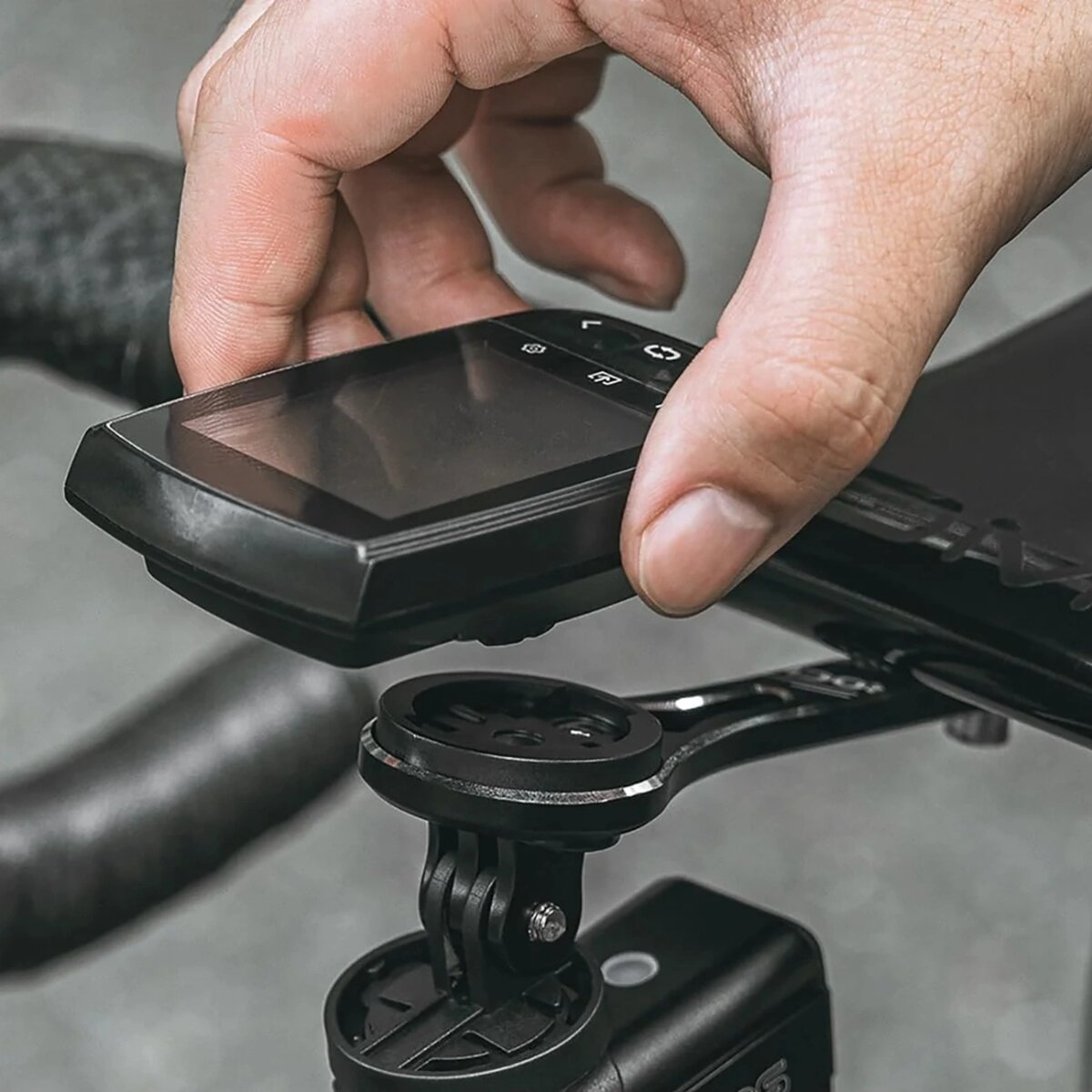 Hand platziert schwarzen Fahrradcomputer auf Lenkerhalterung, grauer Hintergrund.