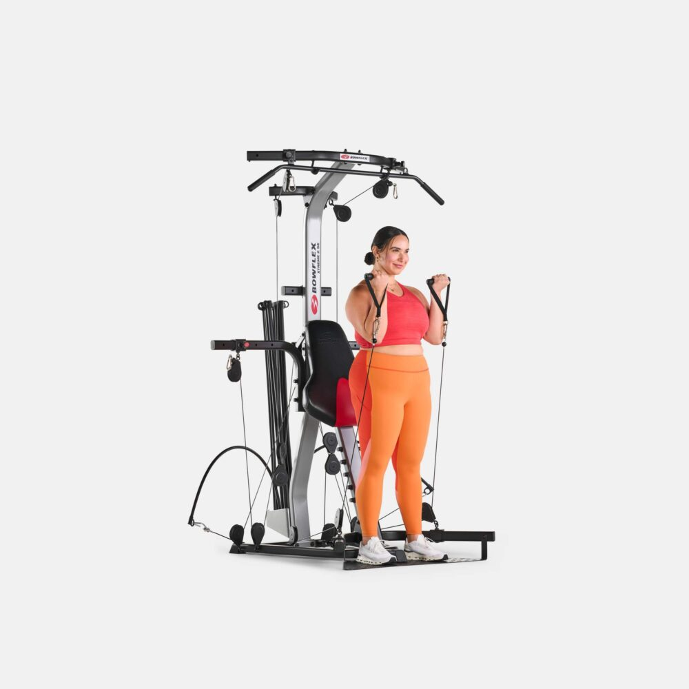 Vrouw in sportkleding traint op een Bowflex-machine in een witte studio.