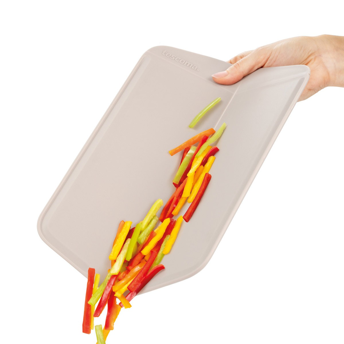 Eine Hand hält ein beiges Schneidebrett mit bunten, gehackten Paprika, die herunterfallen.