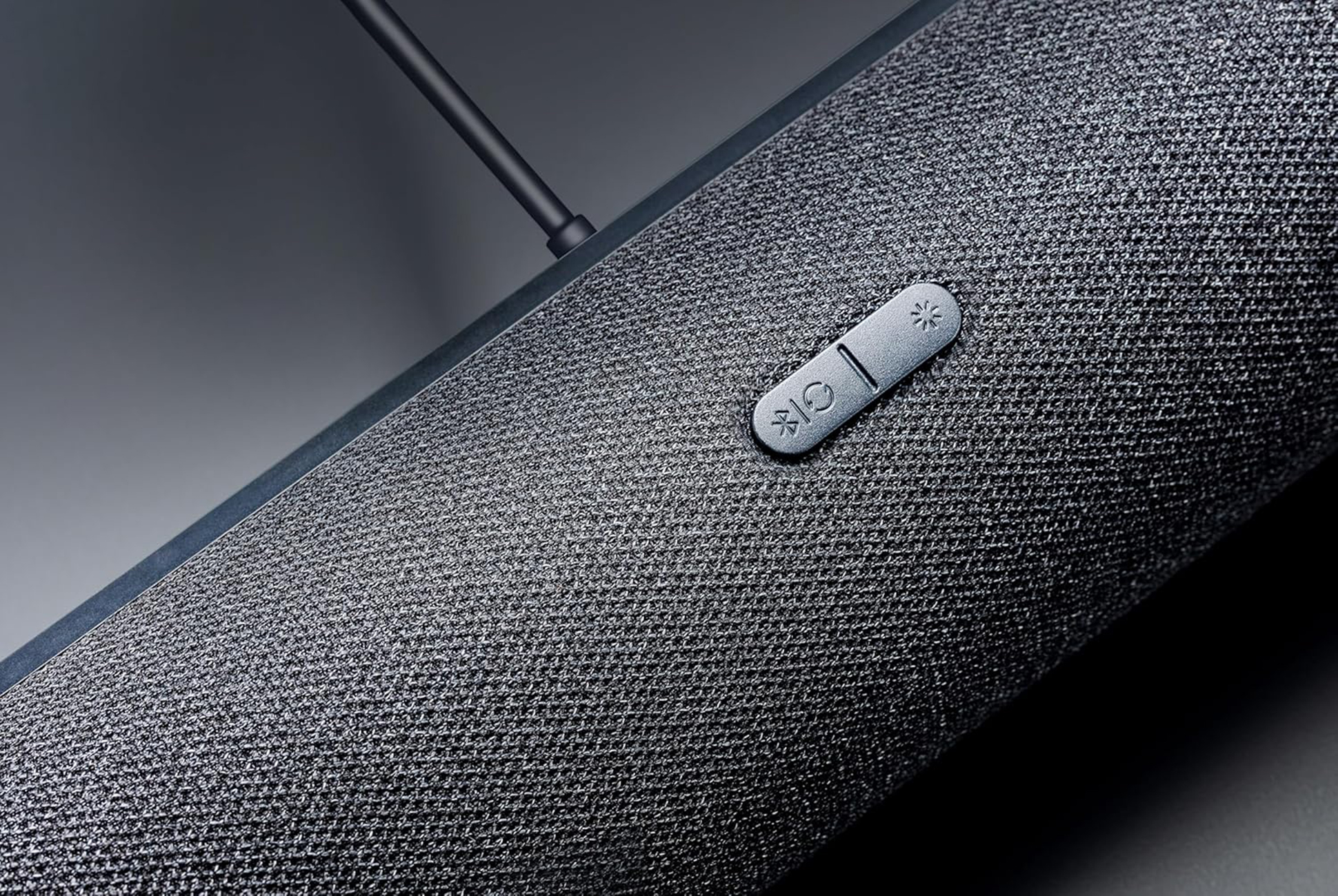 Zbliżenie ciemnoszarego głośnika z przyciskami. Tło jest szare.