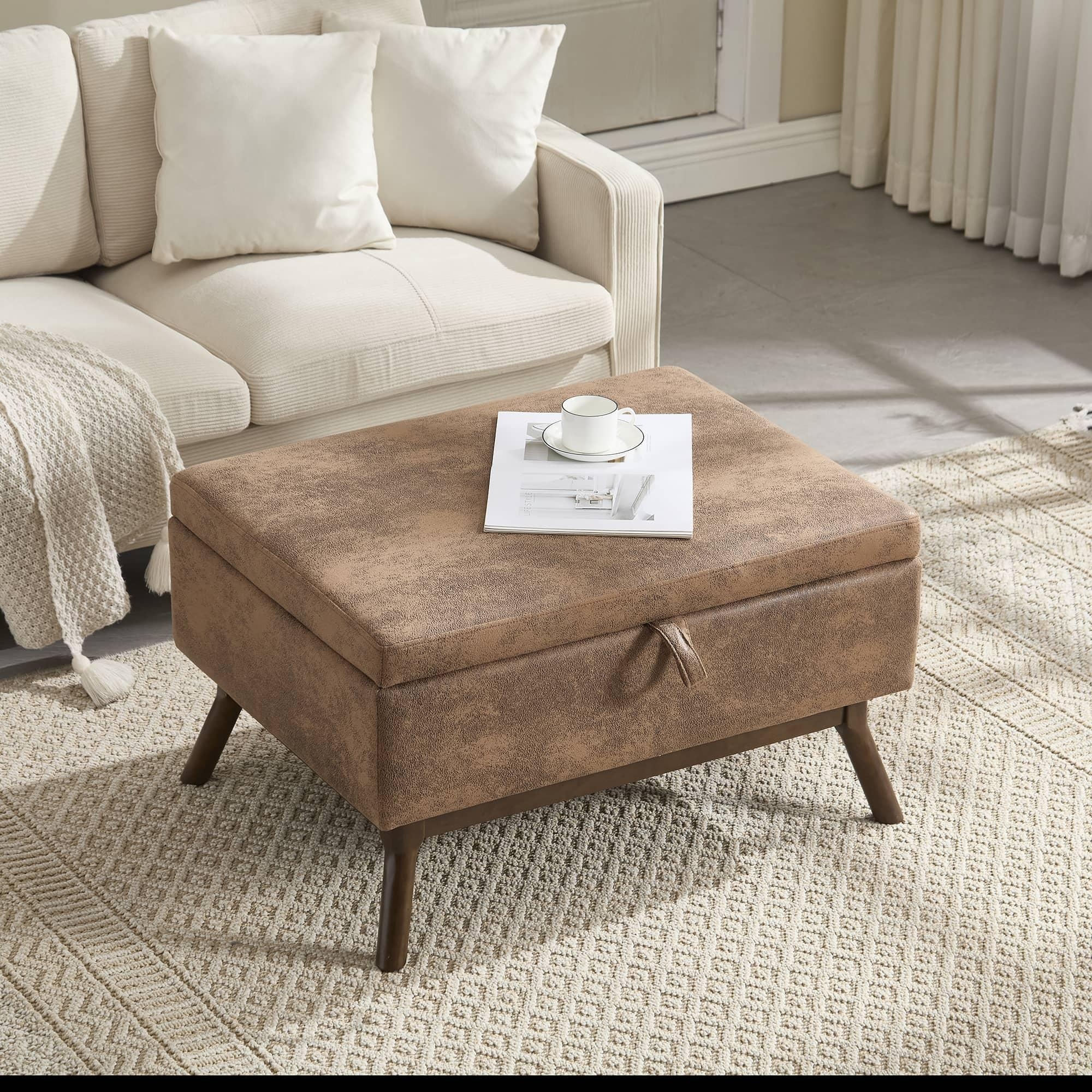 Ein brauner Aufbewahrungshocker mit Deckel. Er steht vor einem weißen Sofa auf einem Teppich. Der Hocker hat Holzbeine.