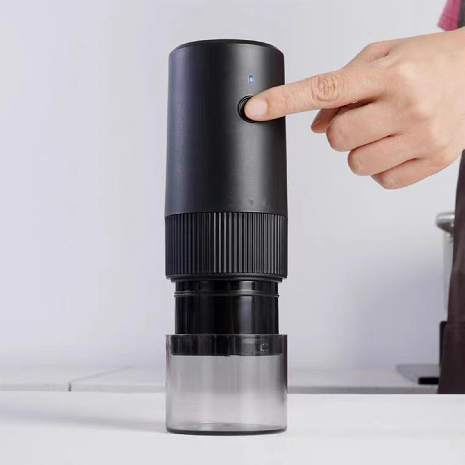 Schwarze elektrische Kaffeemühle. Eine Hand steht kurz davor, den Einschaltknopf zu drücken.