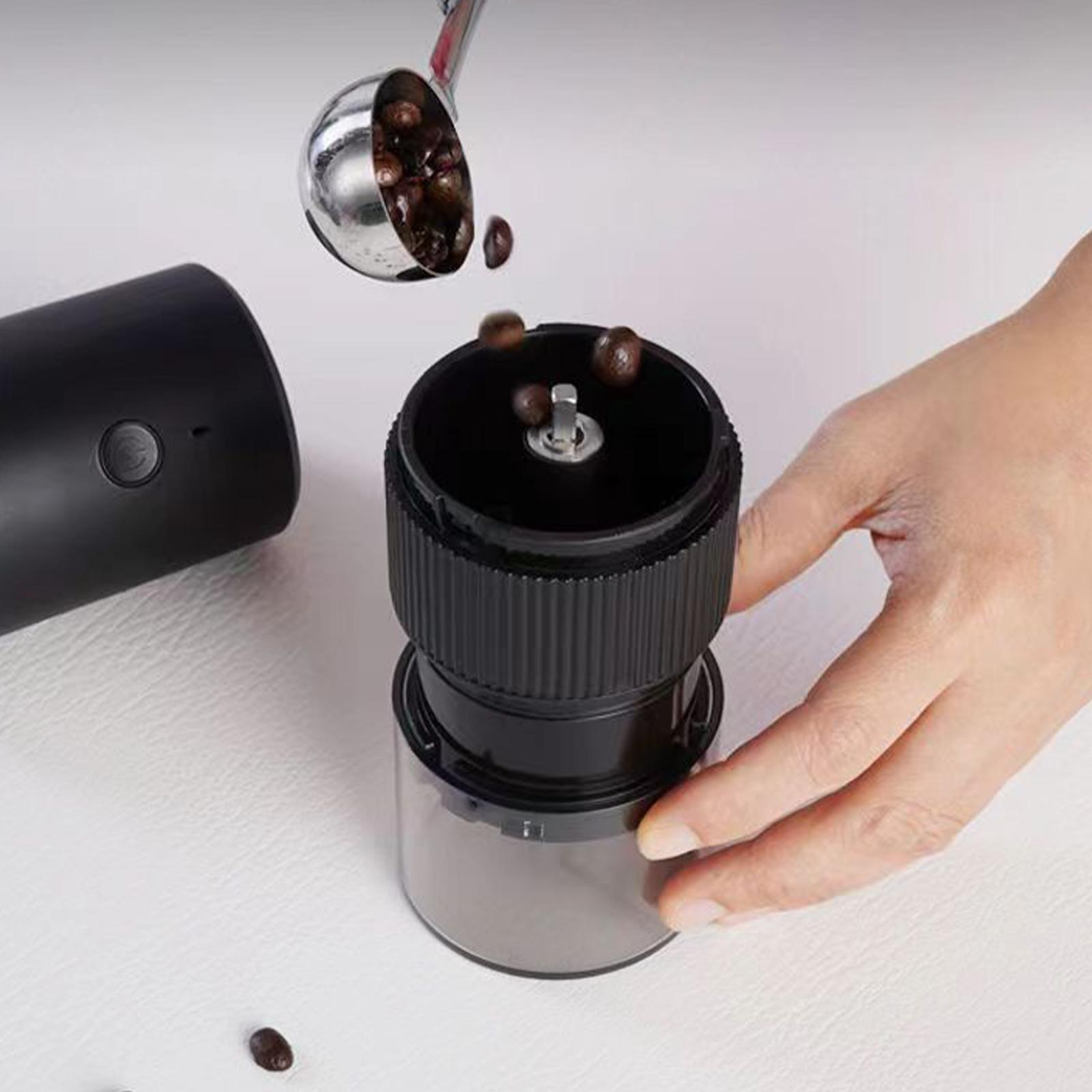 Kaffeebohnen werden mit einer silbernen Schaufel in eine schwarze Kaffeemühle gegossen.