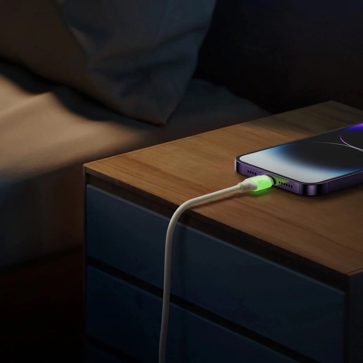 Ein Telefon, das auf einem hölzernen Nachttisch geladen wird. Das Kabel leuchtet grün. Dunkler Raum.