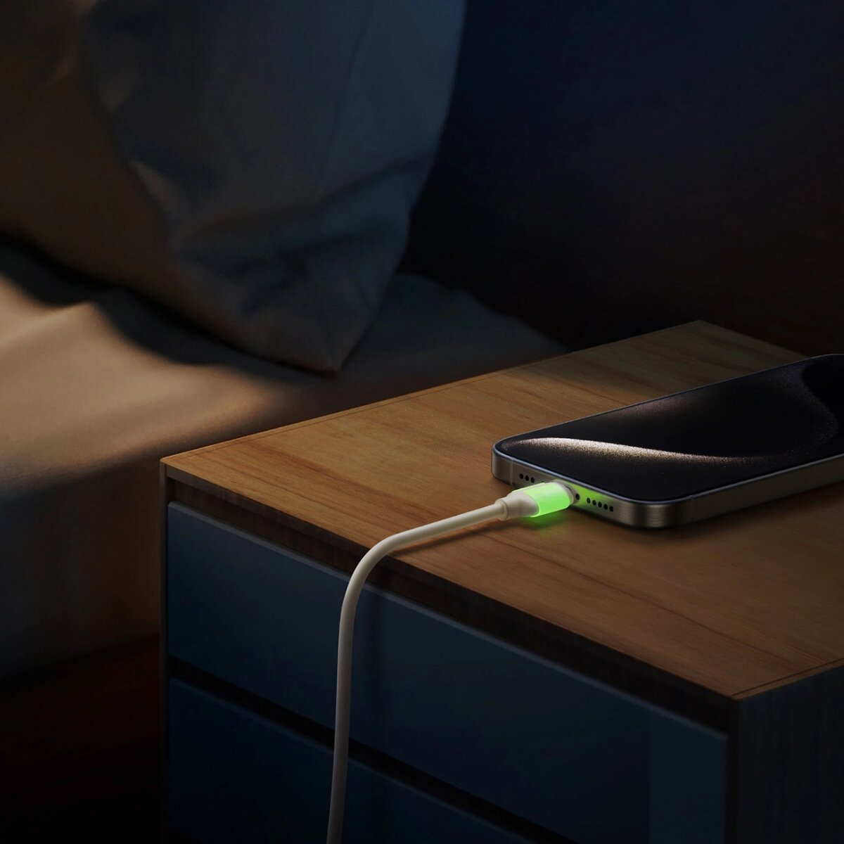 Ein Telefon, das auf einem Nachttisch in einem dunklen Raum geladen wird. Das Kabel leuchtet grün.