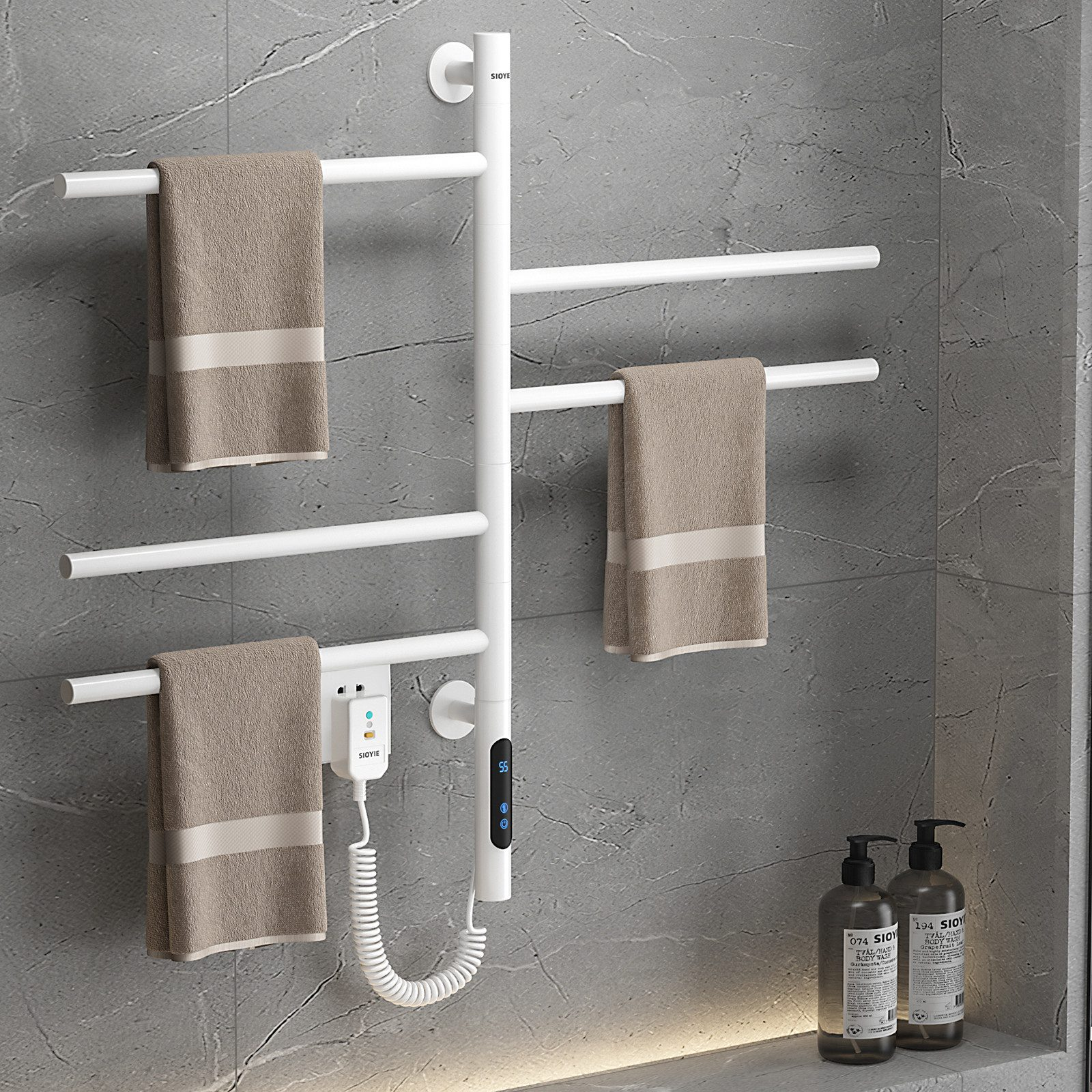 Weißer elektrischer Handtuchwärmer an einer grau gefliesten Wand, mit Handtüchern, Bedienfeld und Seifenflaschen.