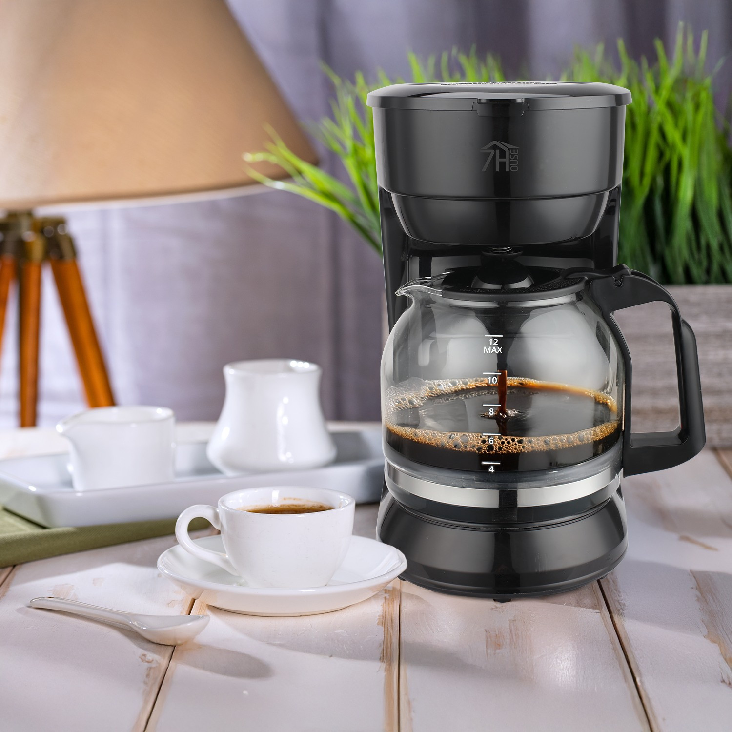Cafetera con jarra de vidrio y una taza de café en una mesa. El fondo está borroso.