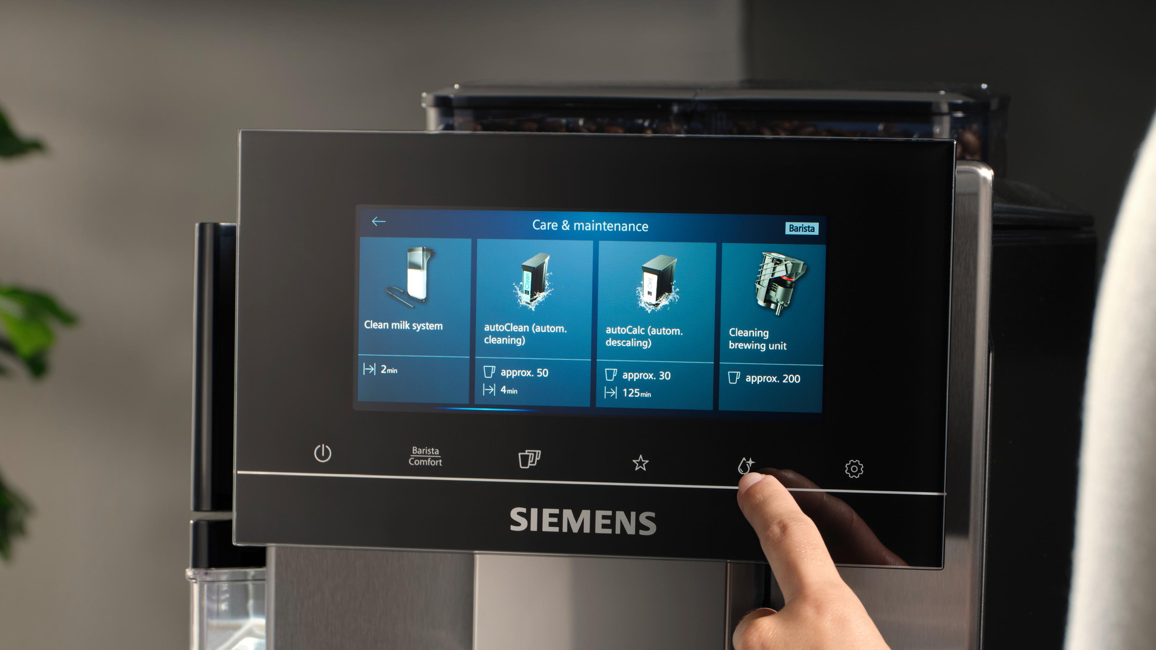 Pantalla de máquina de café mostrando opciones de cuidado y mantenimiento y una mano tocándola.